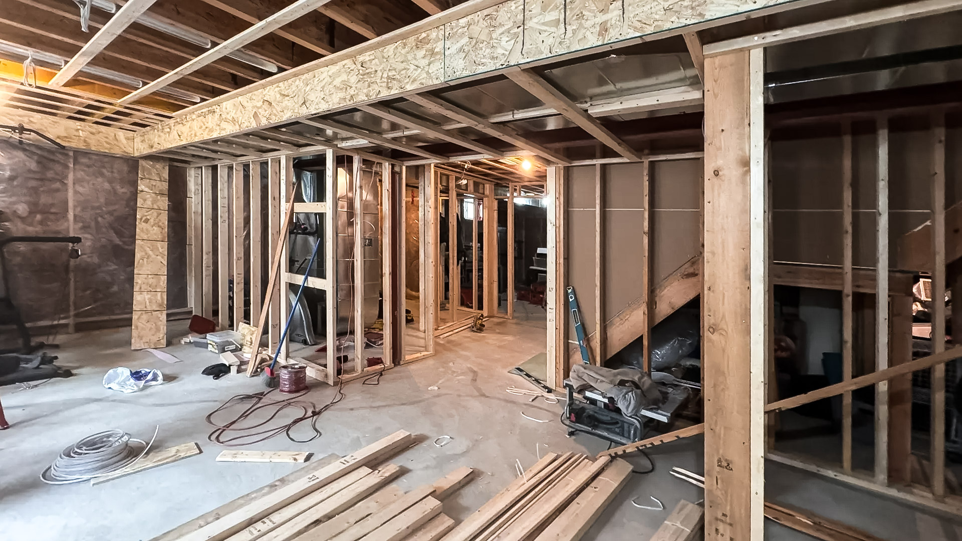Basement under renovation with exposed wooden framing, cables on the floor, and construction tools.