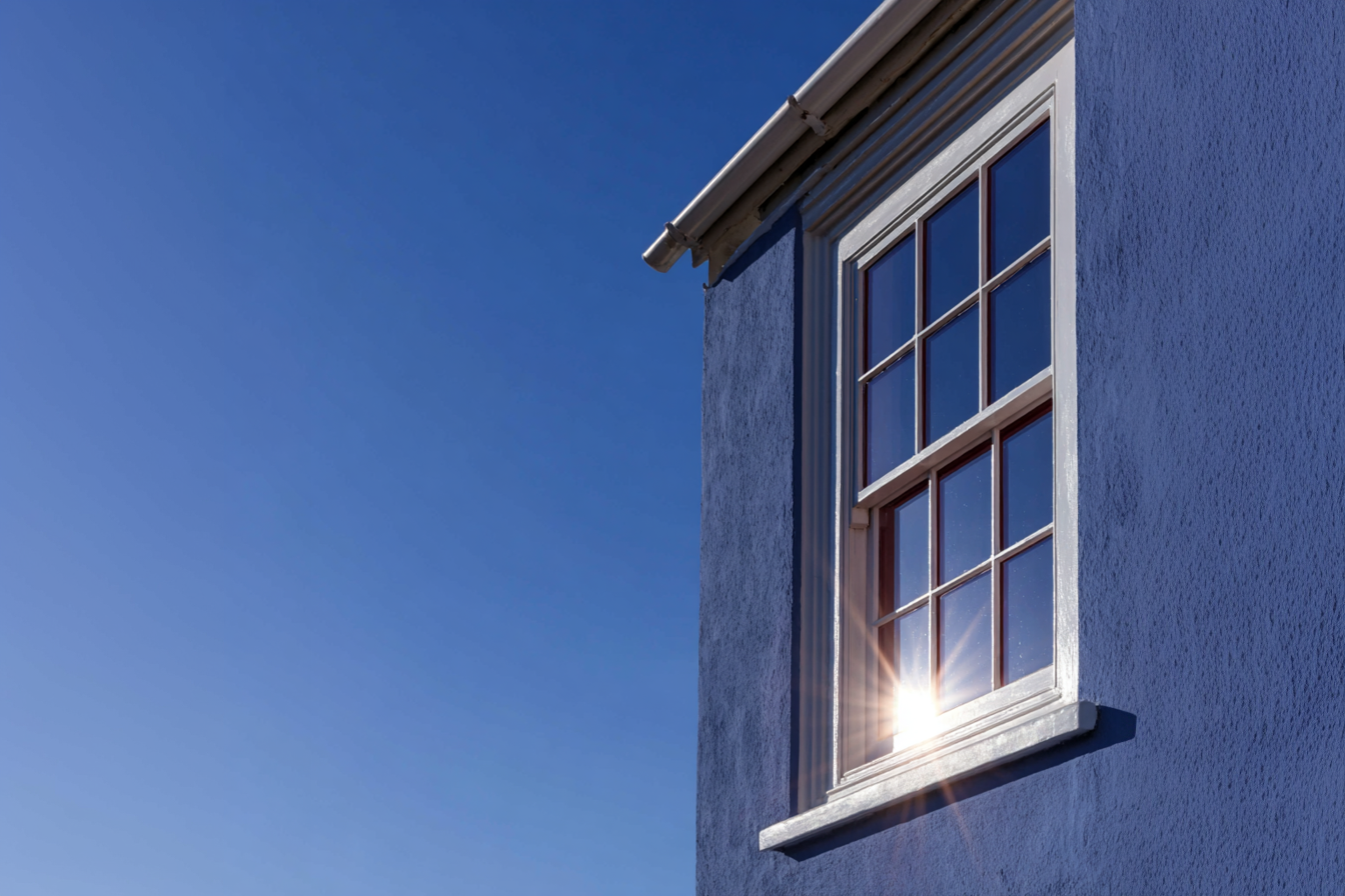 Gridded window on a blue exterior wall with sun reflection and clear sky