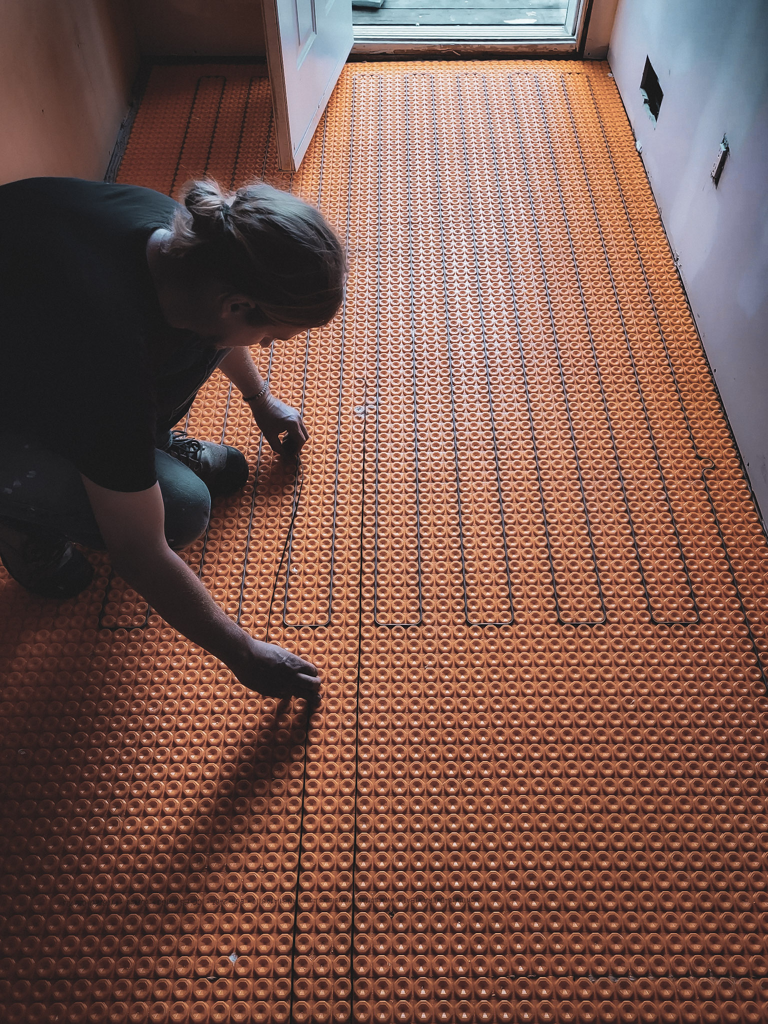 &nbsp;Installation d’un câble chauffant dans une membrane orange pour plancher chauffant électrique, dans une pièce en rénovation.