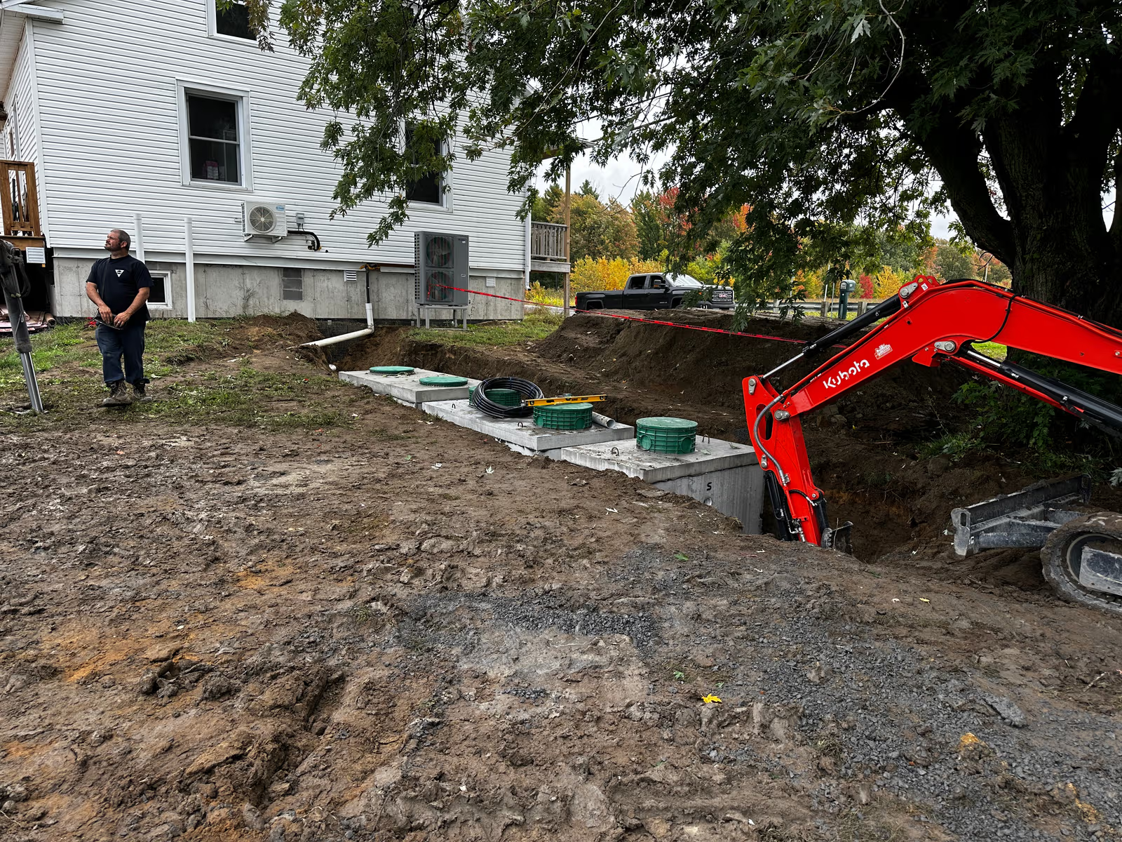 Septic system installation with excavation, mini excavator, access risers and pipes near a residential house