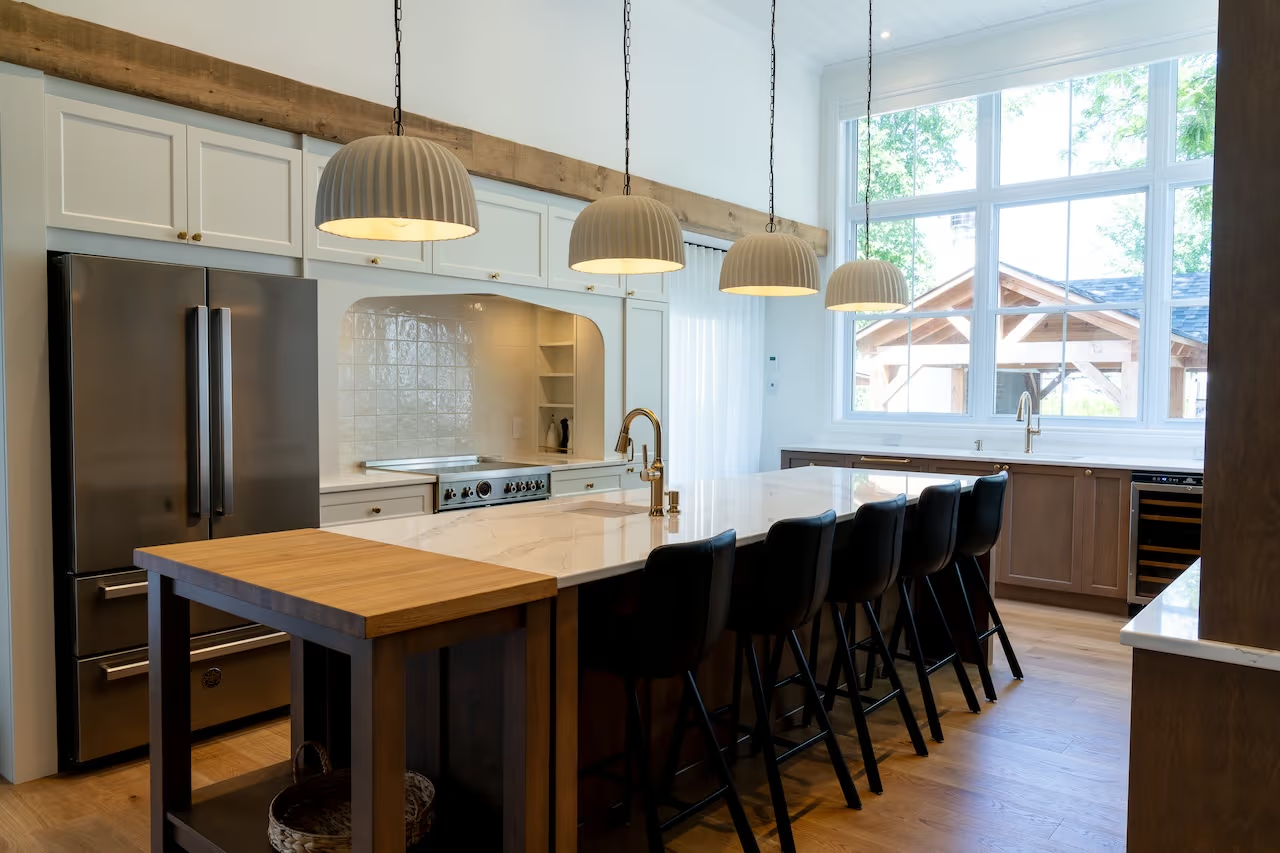 Bright contemporary kitchen with a large central island, quartz countertop, white cabinets, wood accents, pendant lights, and large windows
