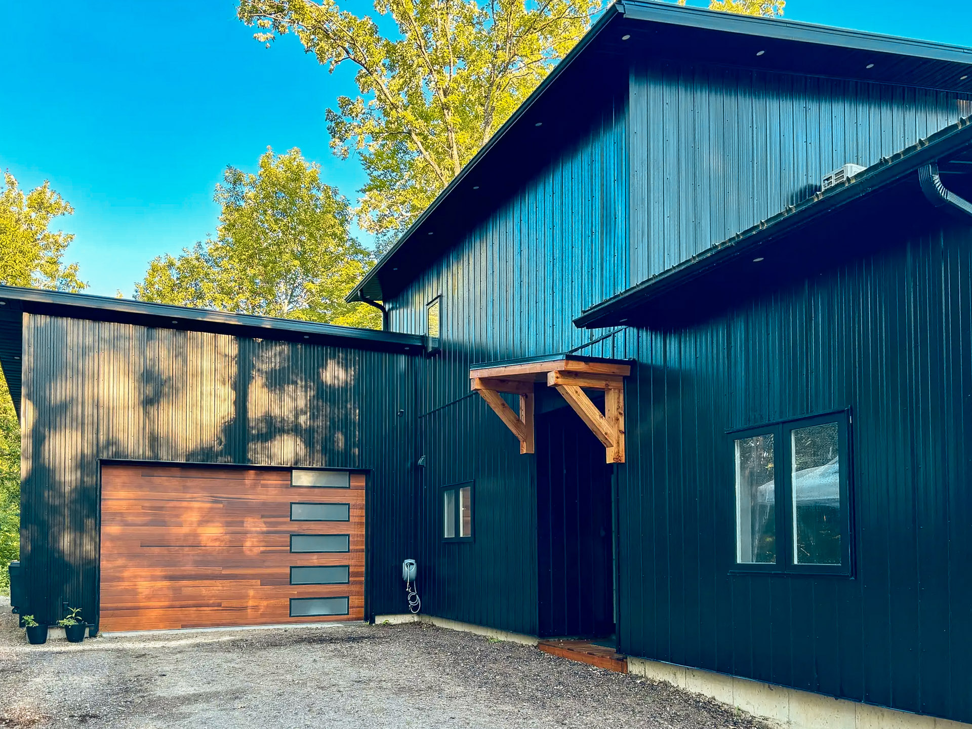 Modern house with black vertical exterior cladding, wooden garage with integrated windows and wooden awning