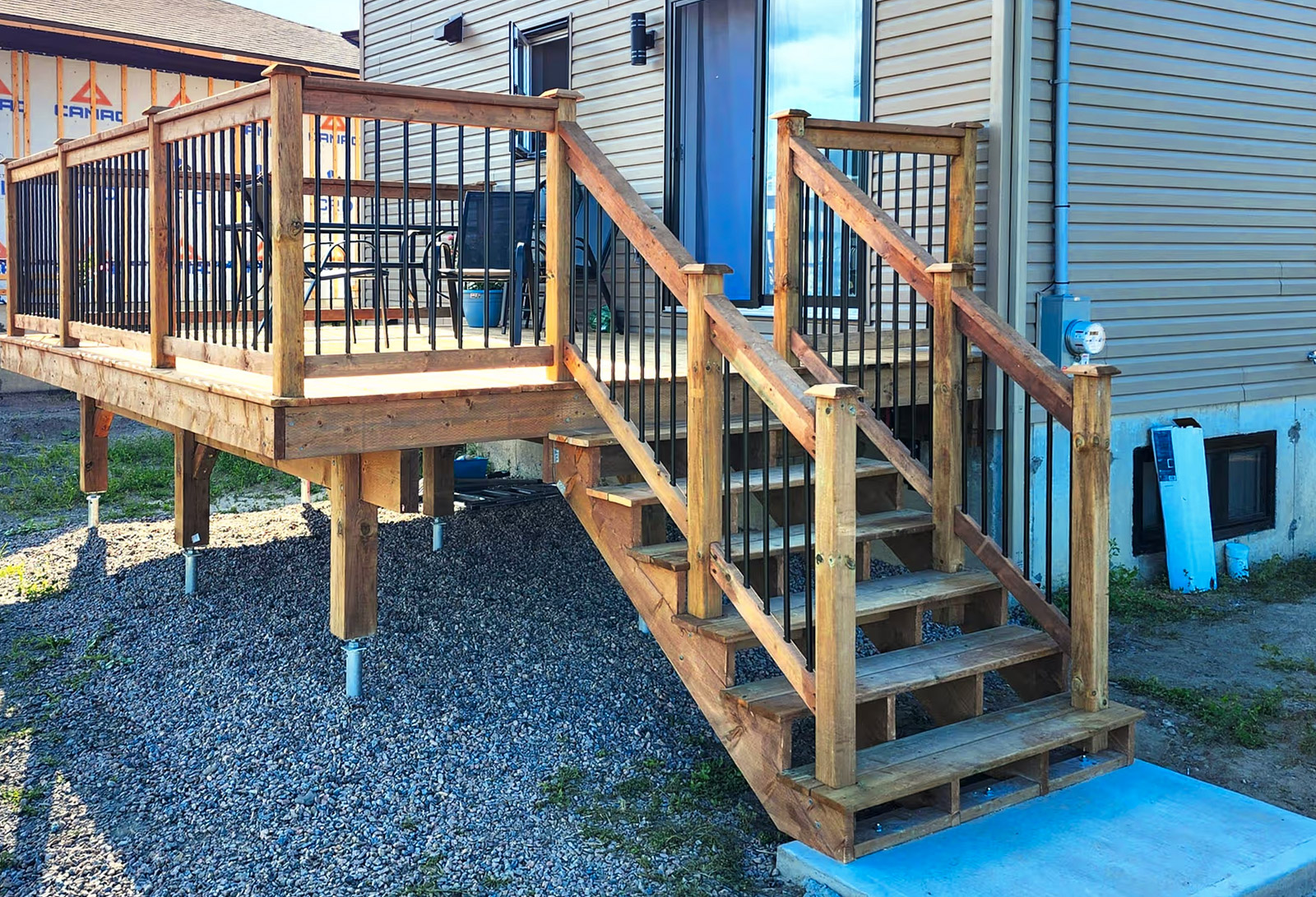 Patio en bois avec escalier, rampes noires et revêtement extérieur de maison résidentielle