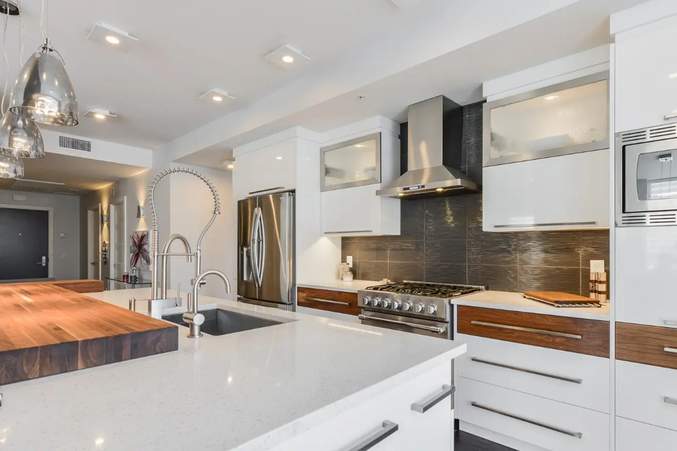 Cuisine moderne avec îlot central en quartz, électroménagers en acier inoxydable et luminaires suspendus pour un design contemporain et épuré.