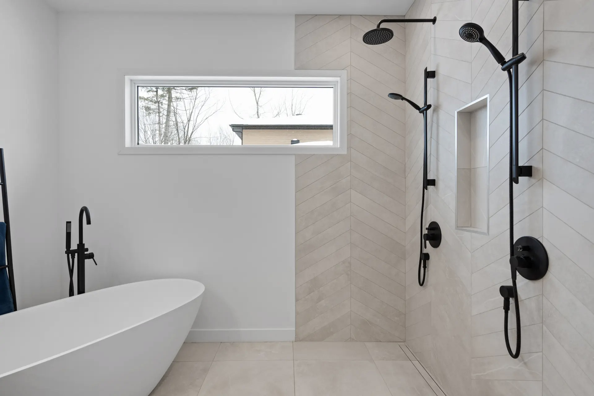 Salle de bain moderne avec douche à l’italienne et carrelage beige en pose chevrons avec robinetterie noire mate