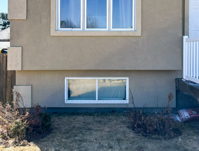 Stucco house facade with triple-section main window and aligned basement window