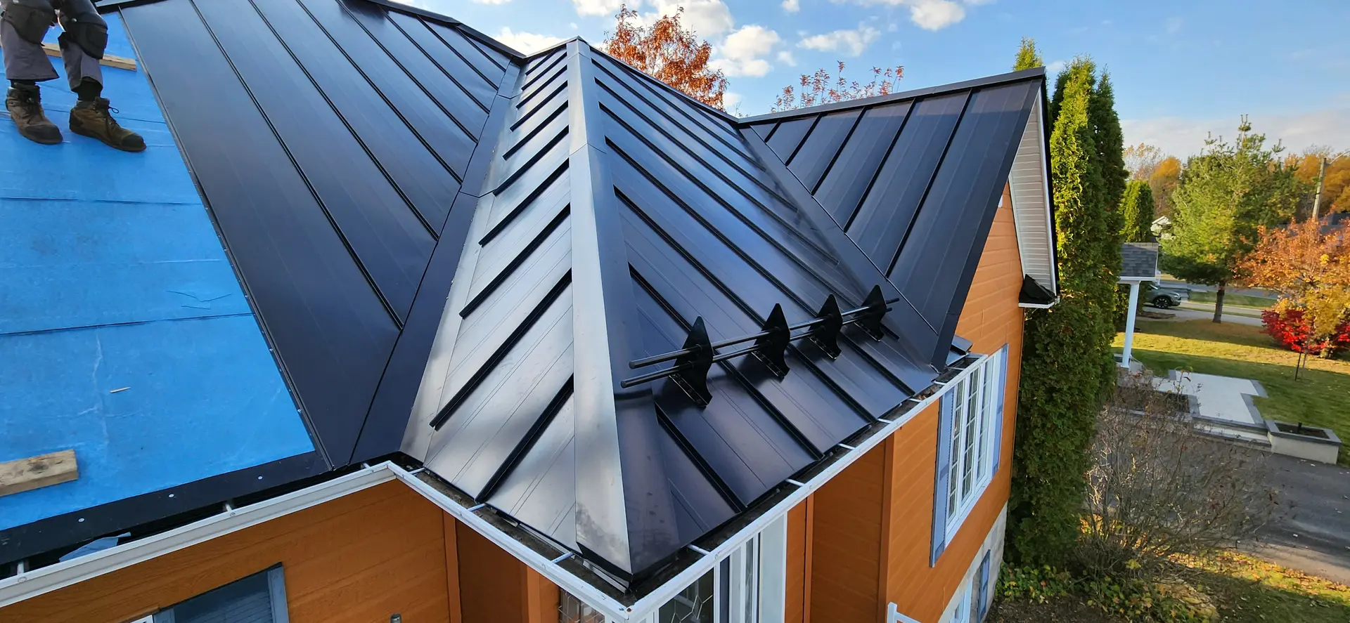 Metal roofing installed on a modern house, featuring black steel panels and a view of a residential neighbourhood.