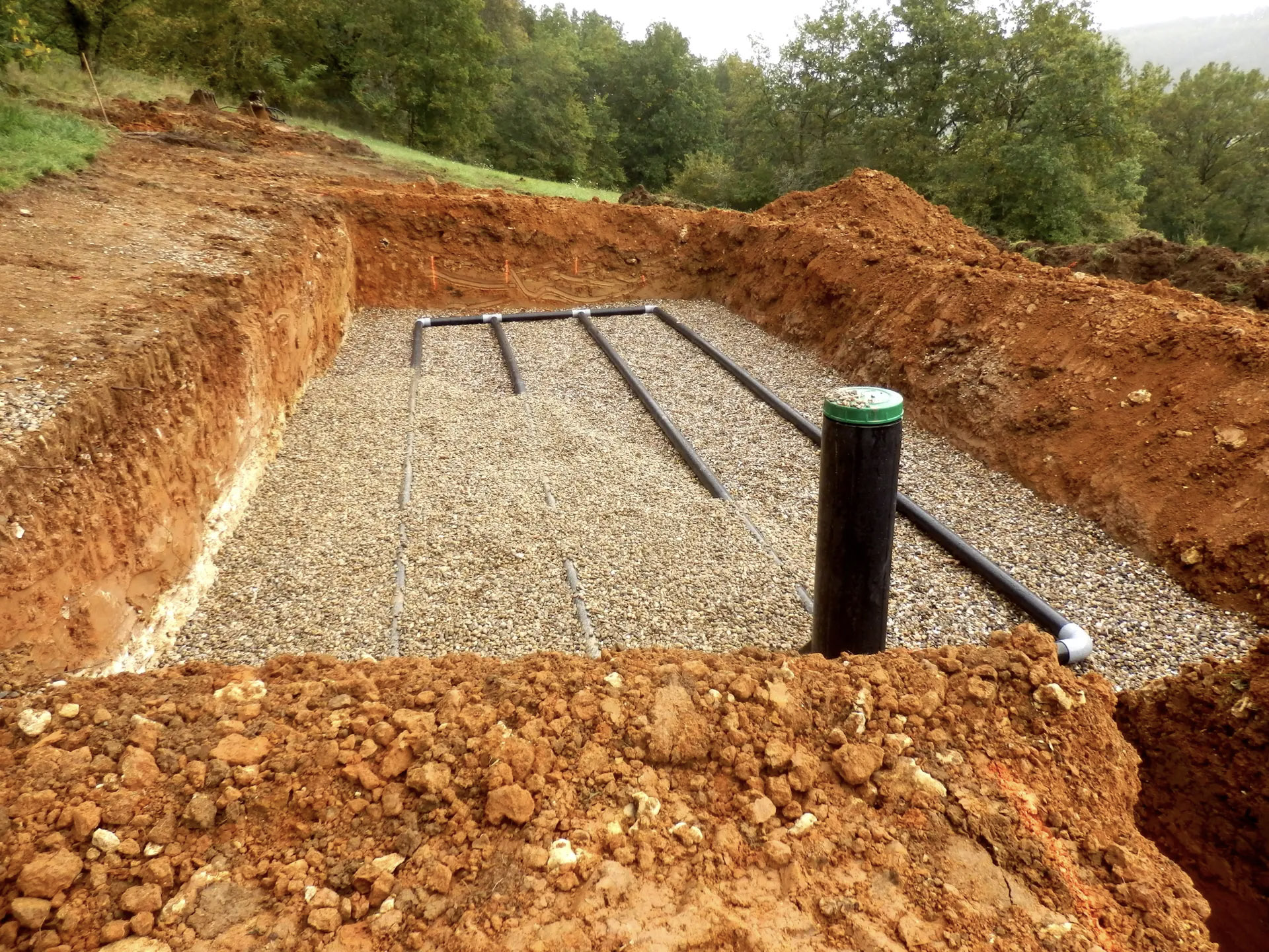 Septic drain field with drainage pipes installed on gravel bed in residential excavation.