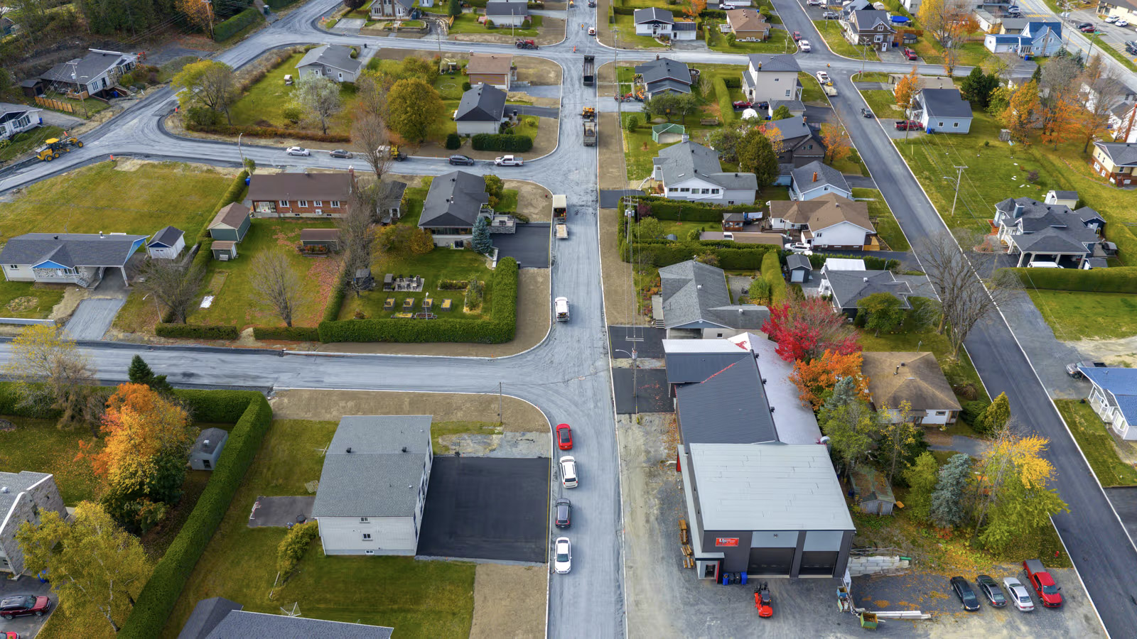 Vue aérienne d’un quartier résidentiel avec maisons, rues fraîchement asphaltées et véhicules de chantier en automne.