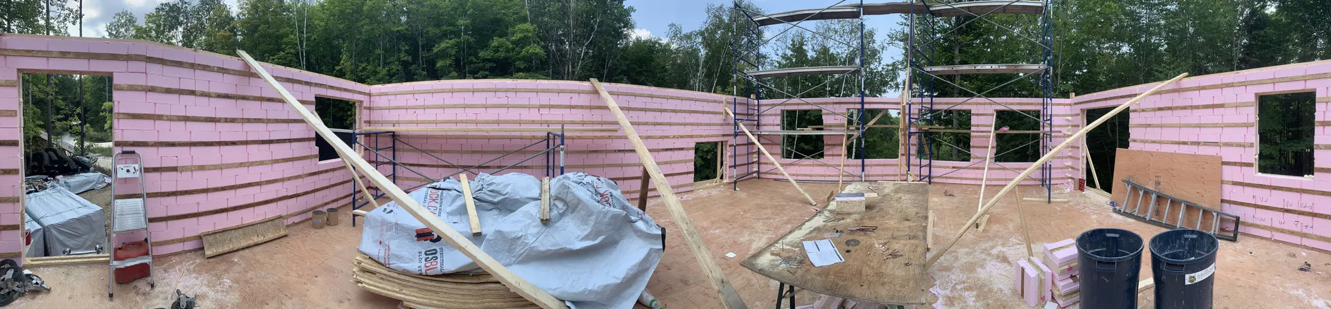Construction site with pink insulated walls, scaffolding, window openings and wood framing.