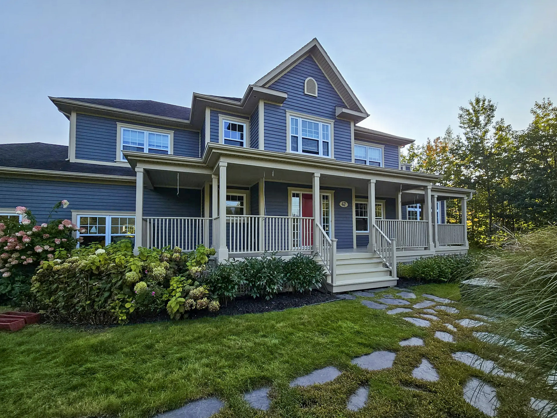 Two-story blue house with front porch and flower landscaping