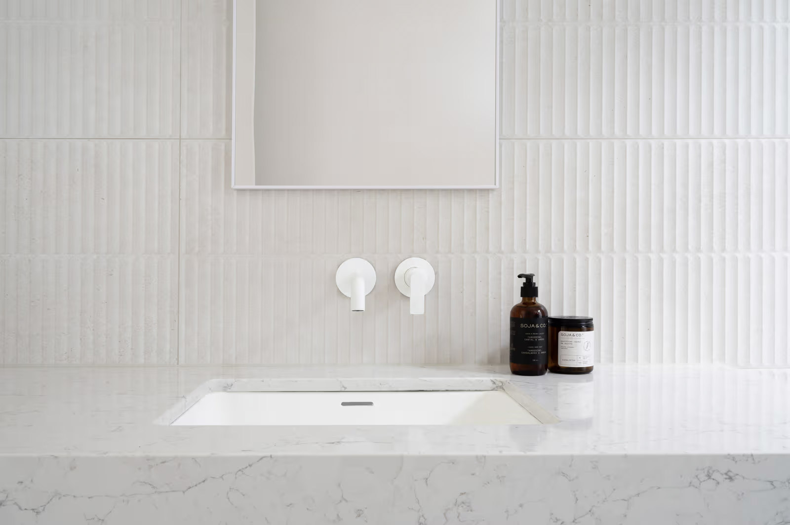 Lavabo moderne encastré en quartz avec robinetterie murale blanche et carrelage texturé dans une salle de bain minimaliste