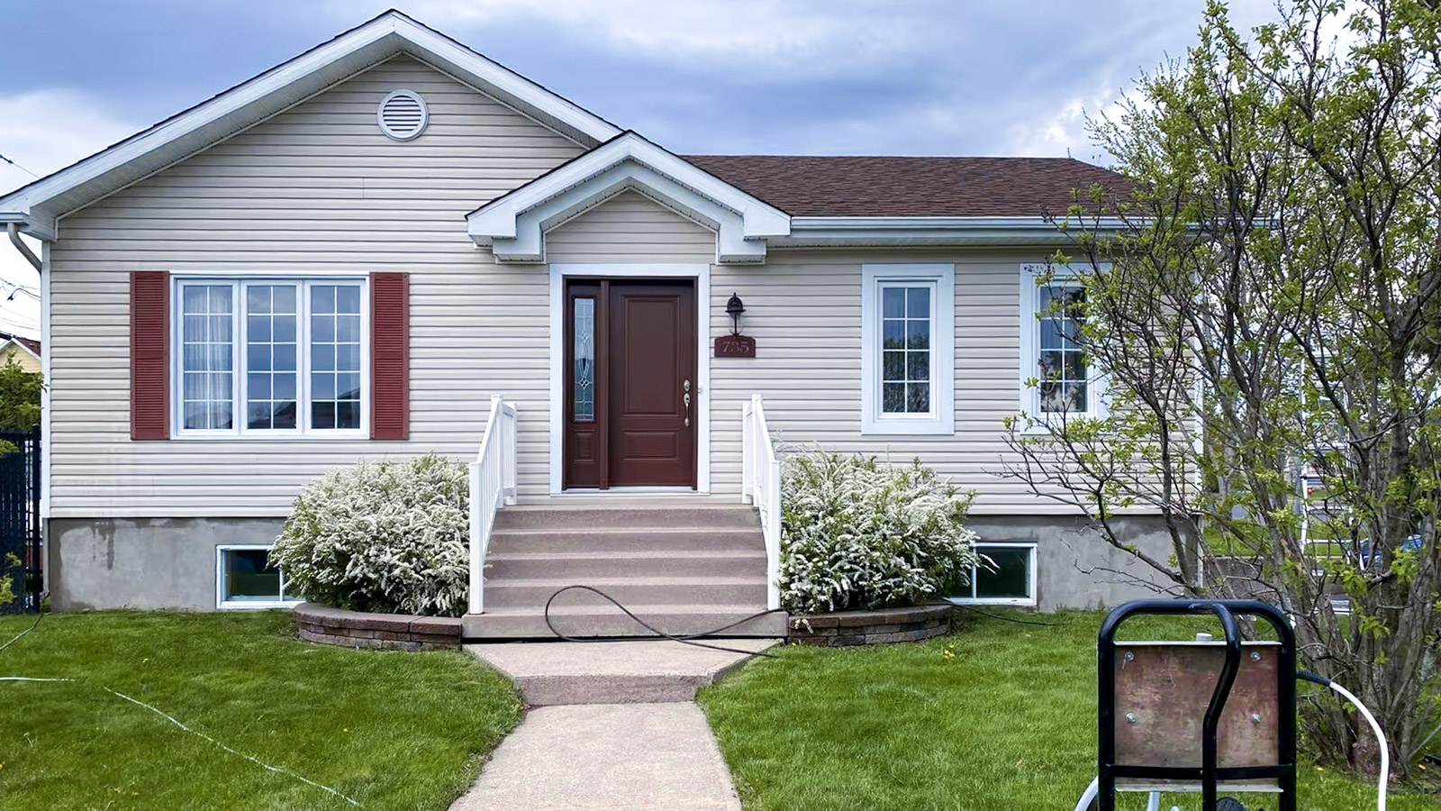 Maison unifamiliale avec revêtement extérieur en vinyle beige, escalier central et aménagement paysager soigné en cour avant