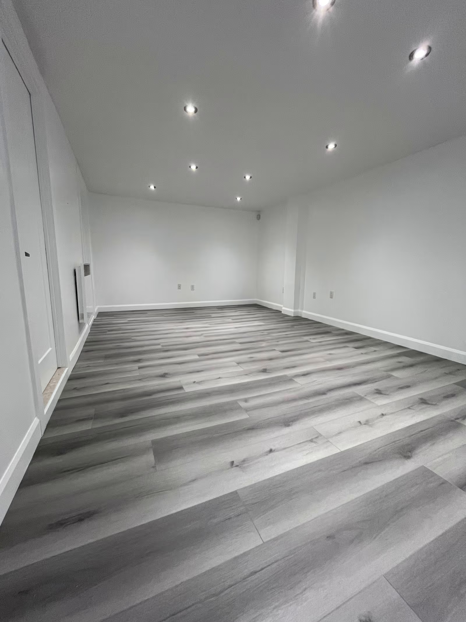 Renovated basement with modern grey laminate flooring, white walls and recessed ceiling lighting