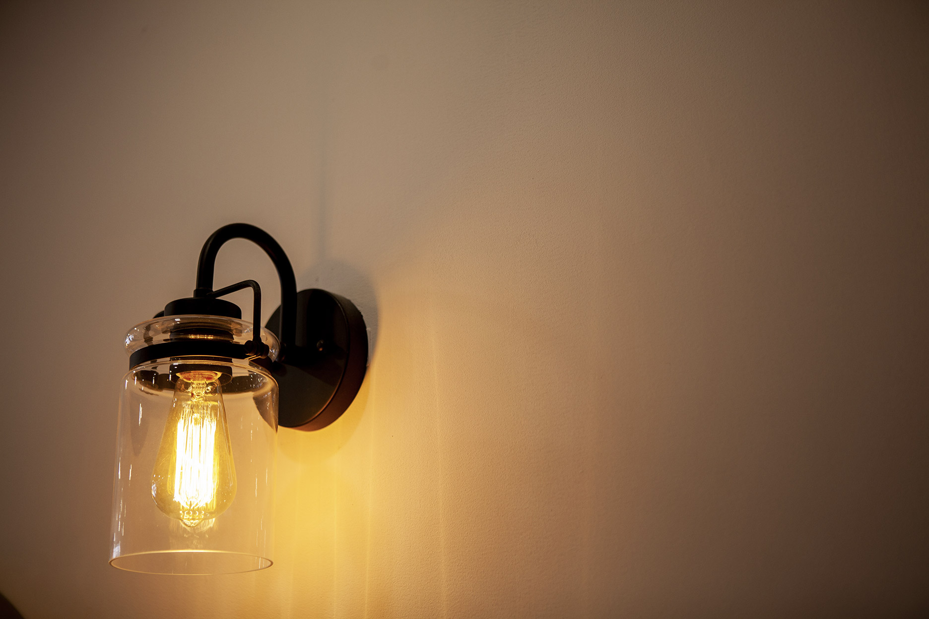 Modern wall sconce with a black fixture, clear glass shade, and exposed filament bulb providing warm ambient lighting.