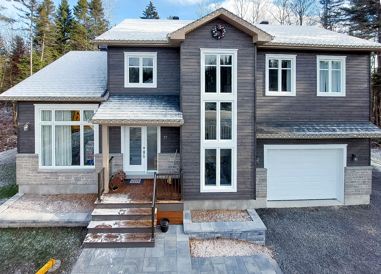 Maison unifamiliale moderne avec revêtement extérieur en bois, garage intégré et aménagement paysager en façade