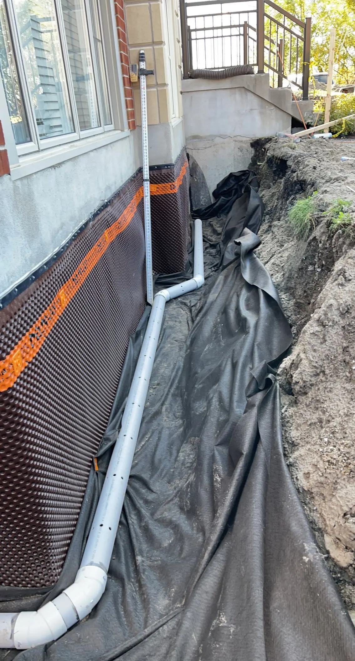 Installation of a French drain with a waterproofing membrane on a house foundation.