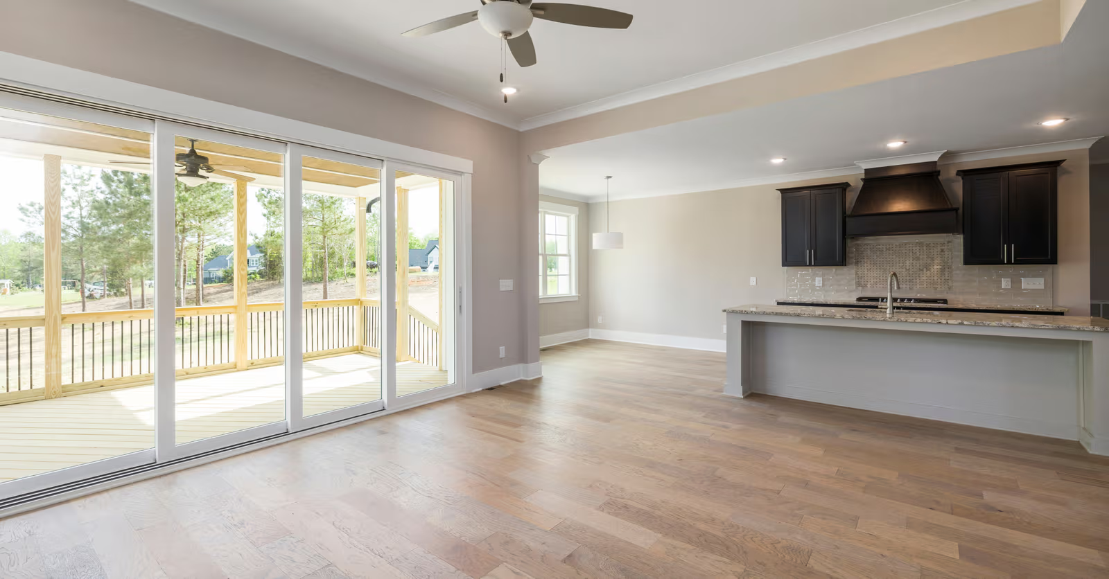 Aire ouverte rénovée avec plancher de bois, cuisine moderne, îlot avec comptoir, portes patio vitrées et balcon couvert en bois.