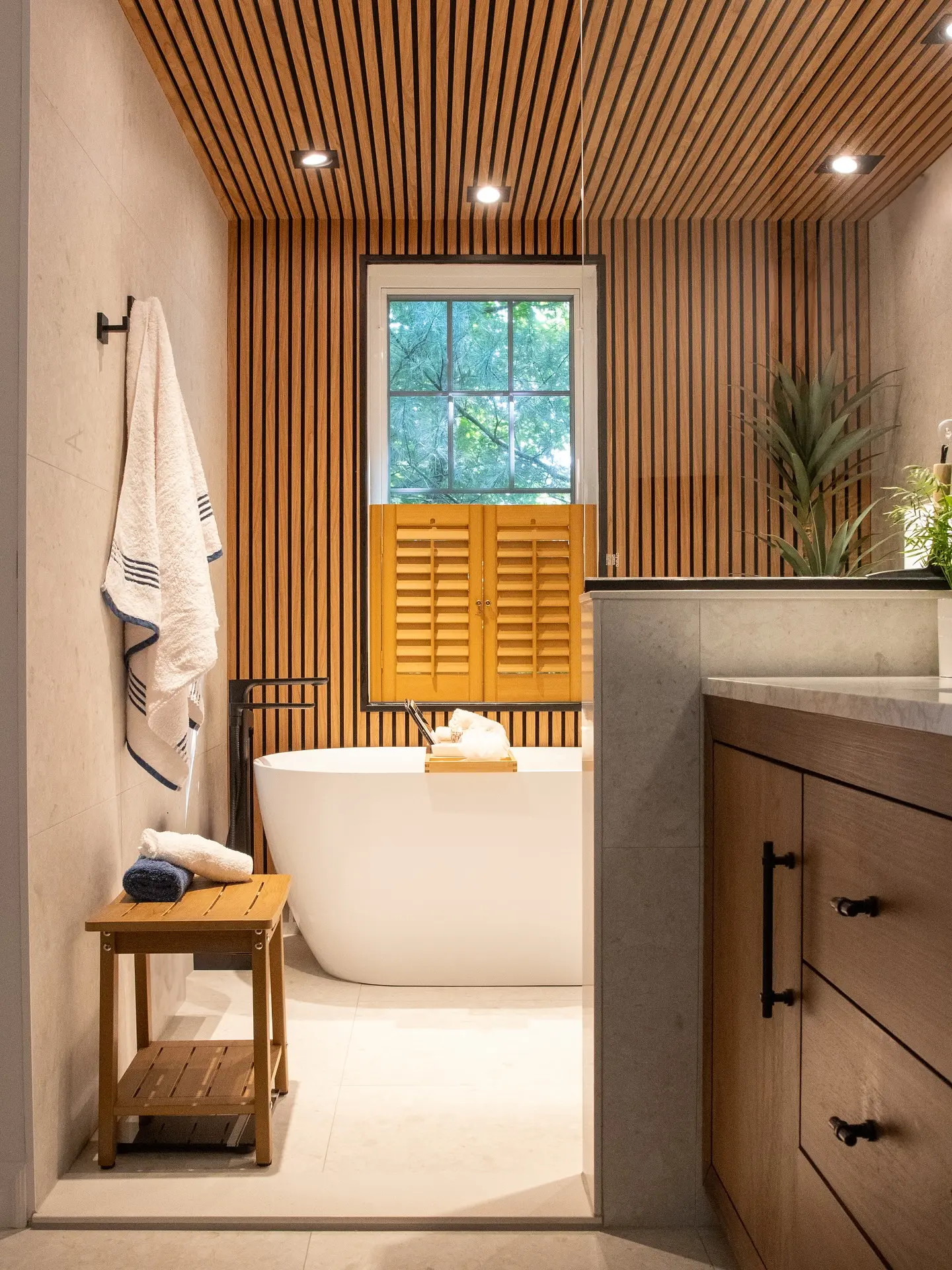 Modern bathroom with freestanding bathtub, wood slat ceiling, wooden vanity and recessed lighting