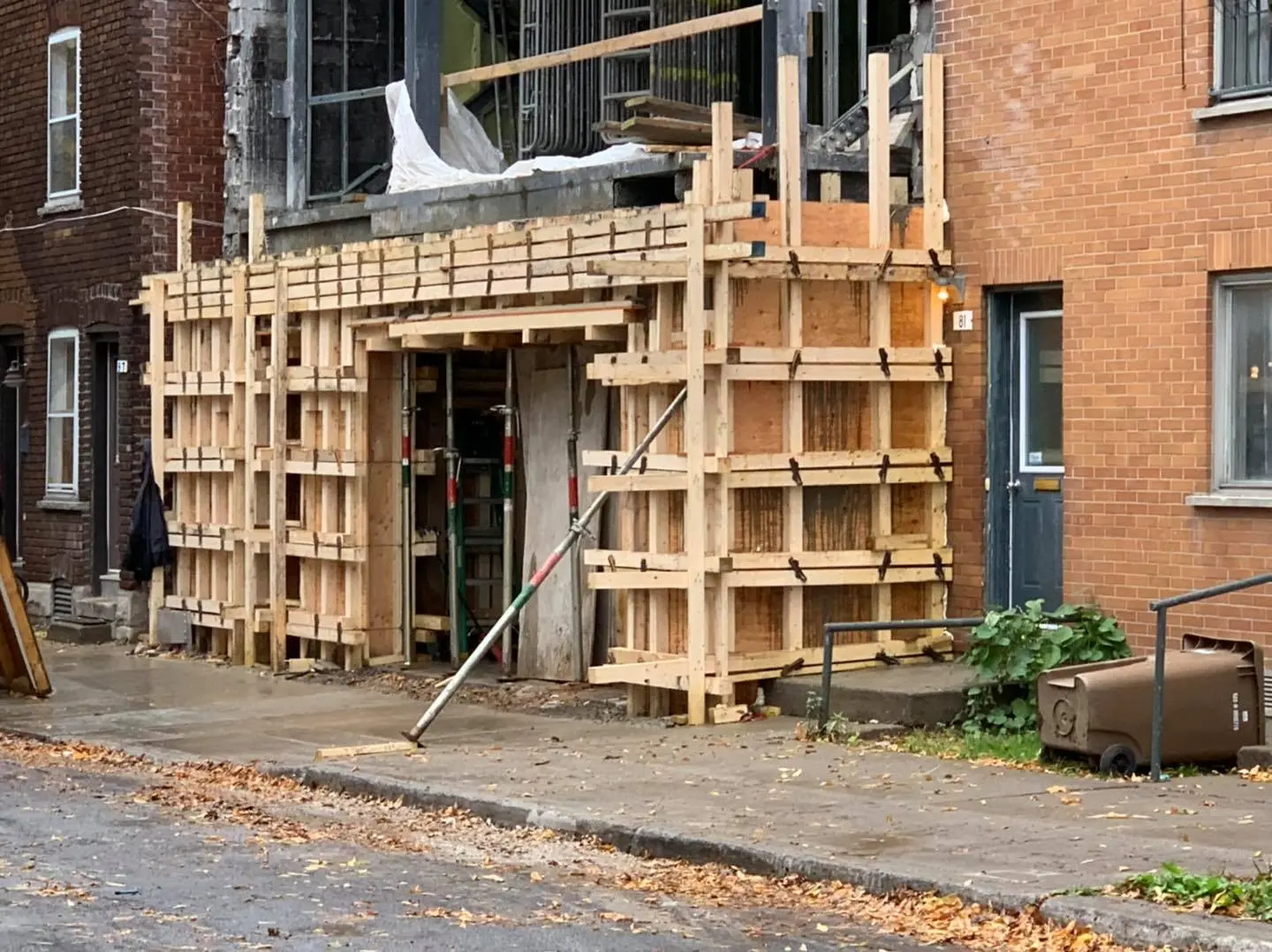 Building facade under renovation with wooden concrete formwork and temporary structure on urban sidewalk