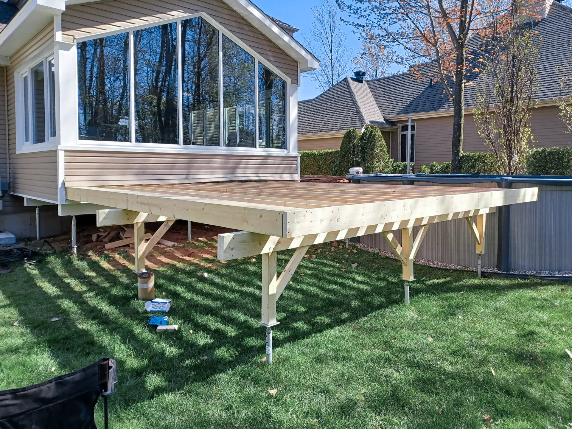 Structure de patio en bois en construction adossée à une maison avec solarium vitré et piscine hors terre