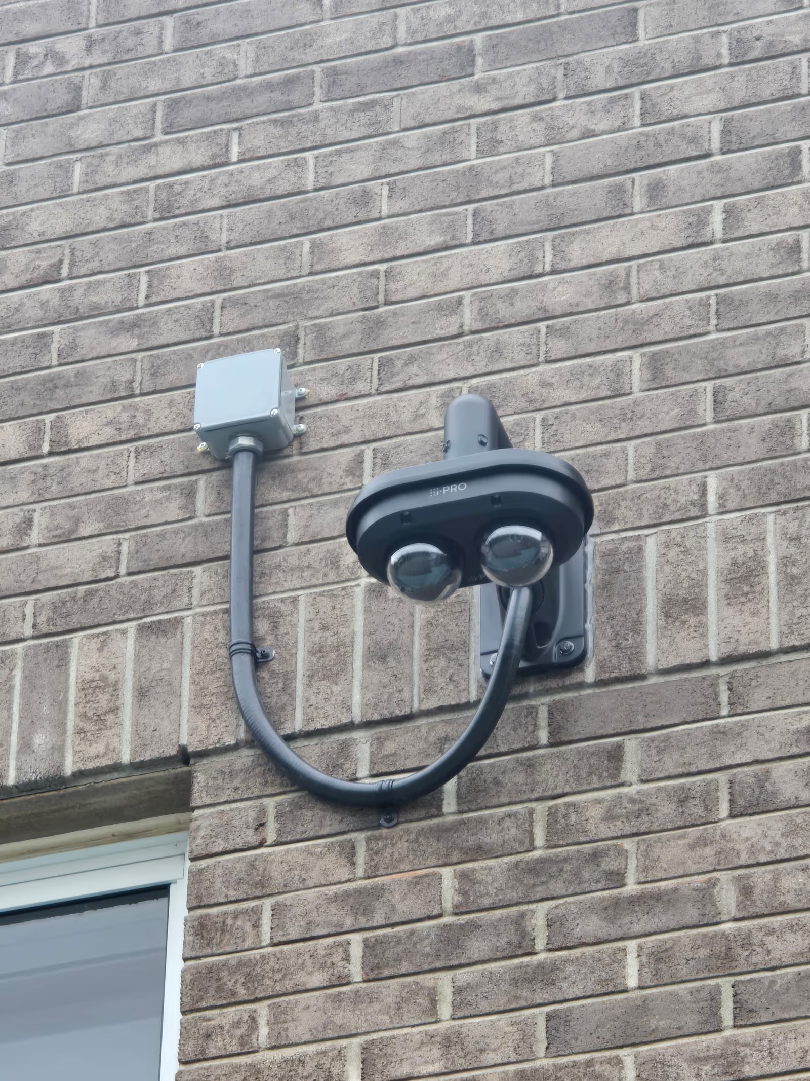 Professional outdoor security camera installed on a brick wall with electrical junction box and exposed conduit for residential surveillance