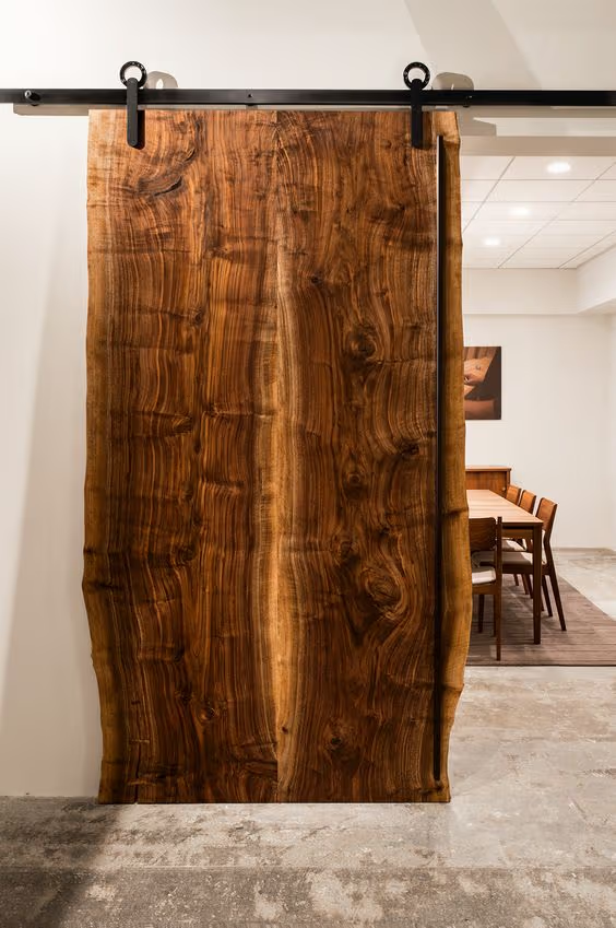 Porte coulissante en bois massif à bord naturel avec rail noir, apportant un style rustique et chaleureux à l’intérieur.