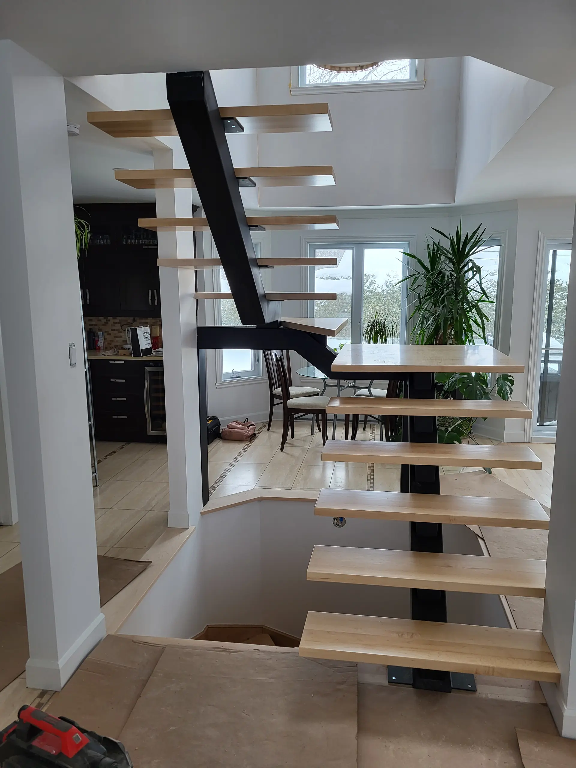 Modern floating staircase with light wood treads, black metal central stringer and bright open-concept interior dining area