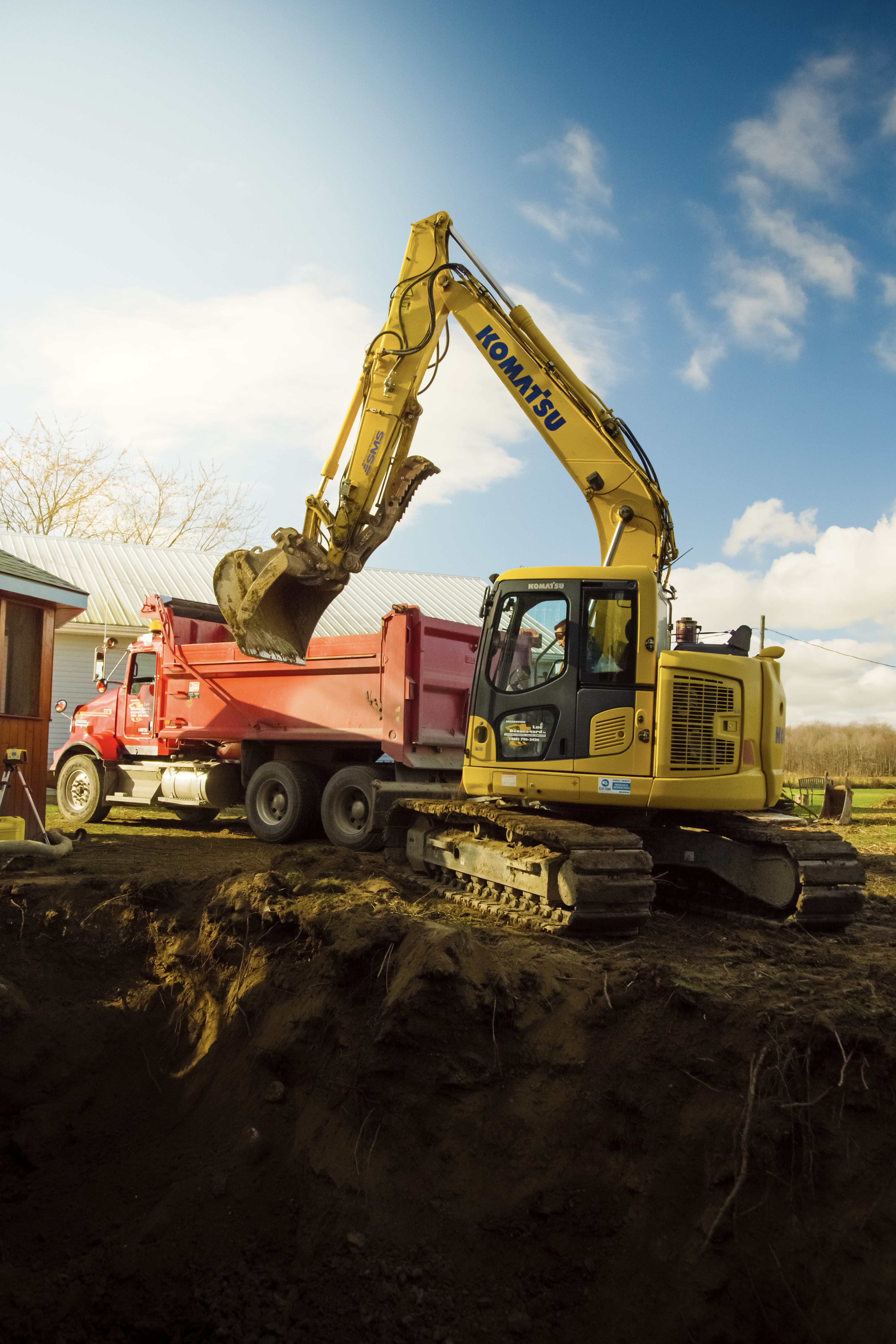 &nbsp;Pelle mécanique Komatsu chargeant de la terre dans un camion-benne rouge sur un chantier résidentiel