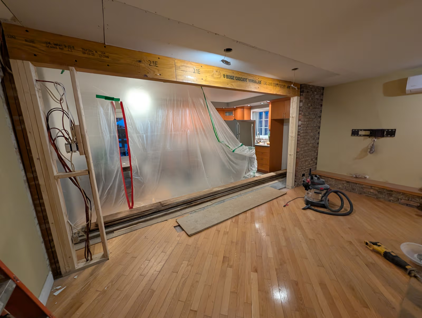 Ouverture de mur porteur avec poutre en bois, câblage apparent et zone de cuisine protégée par une bâche