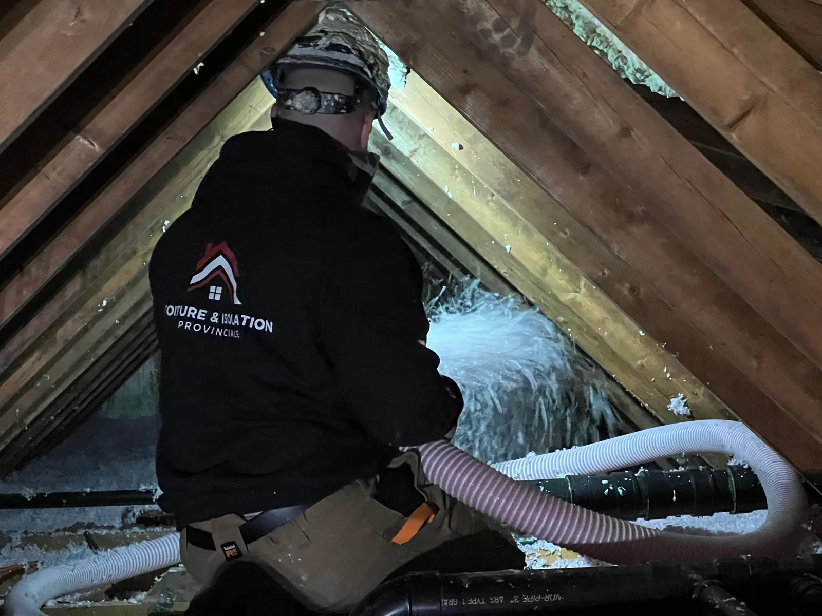 Worker blowing loose-fill insulation into a dark attic using a flexible hose to improve energy efficiency