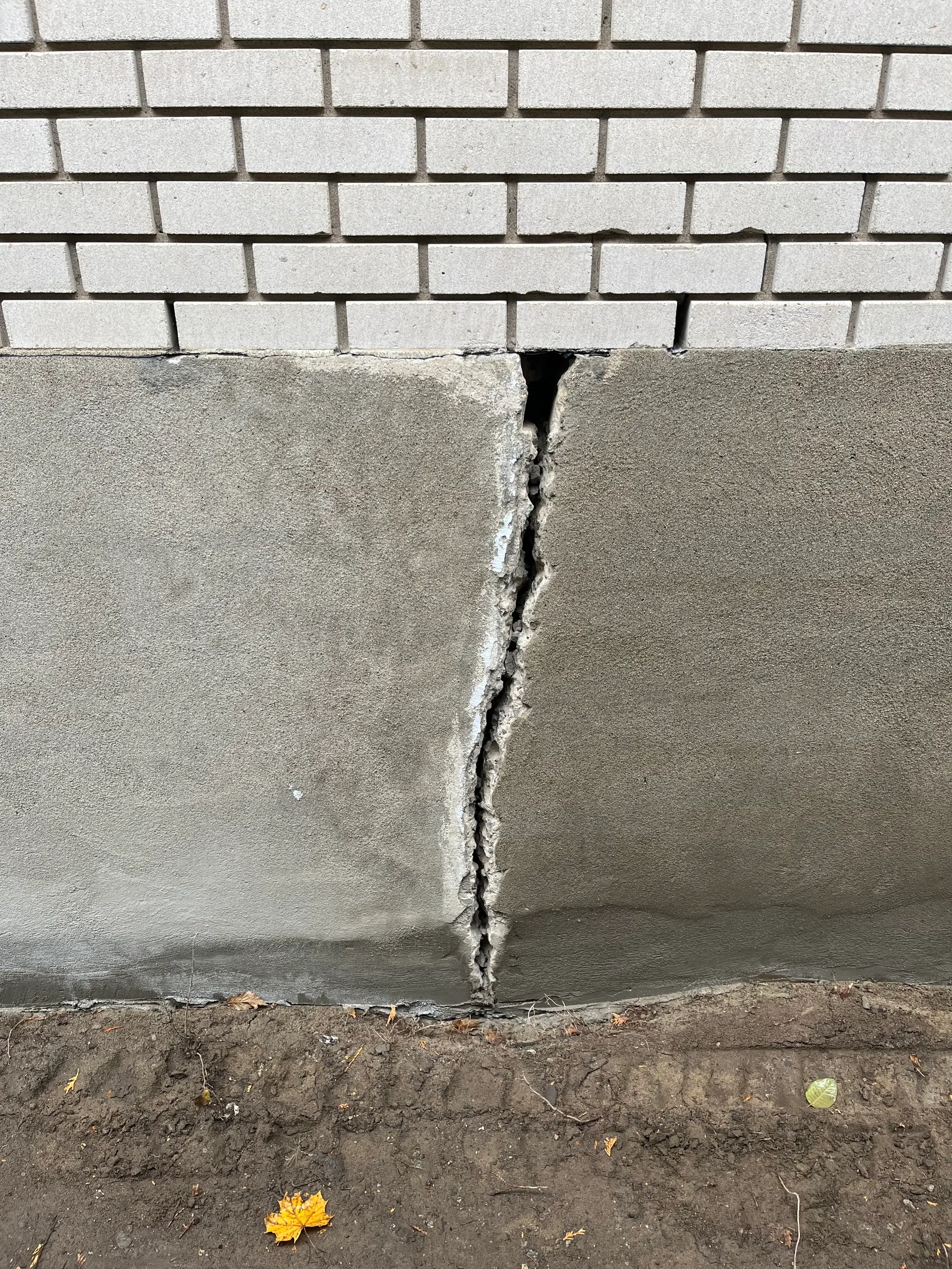 Large vertical crack in a concrete foundation beneath a brick wall, requiring inspection and repair work.
