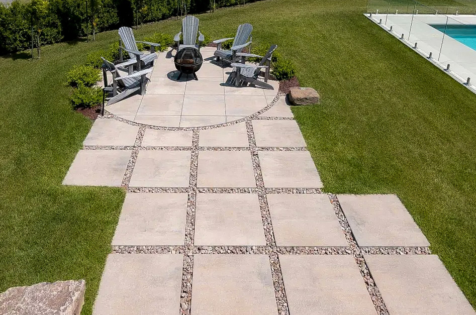 Terrasse extérieure moderne en pavés avec foyer central et chaises Adirondack sur pelouse entretenue
