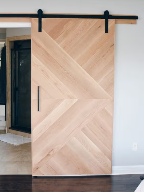 Porte coulissante moderne en bois clair avec motif chevron, rail noir et poignée minimaliste dans un intérieur contemporain.