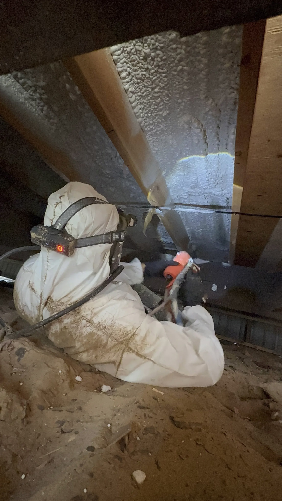 Worker in protective clothing applying spray foam insulation in an attic to improve energy efficiency.