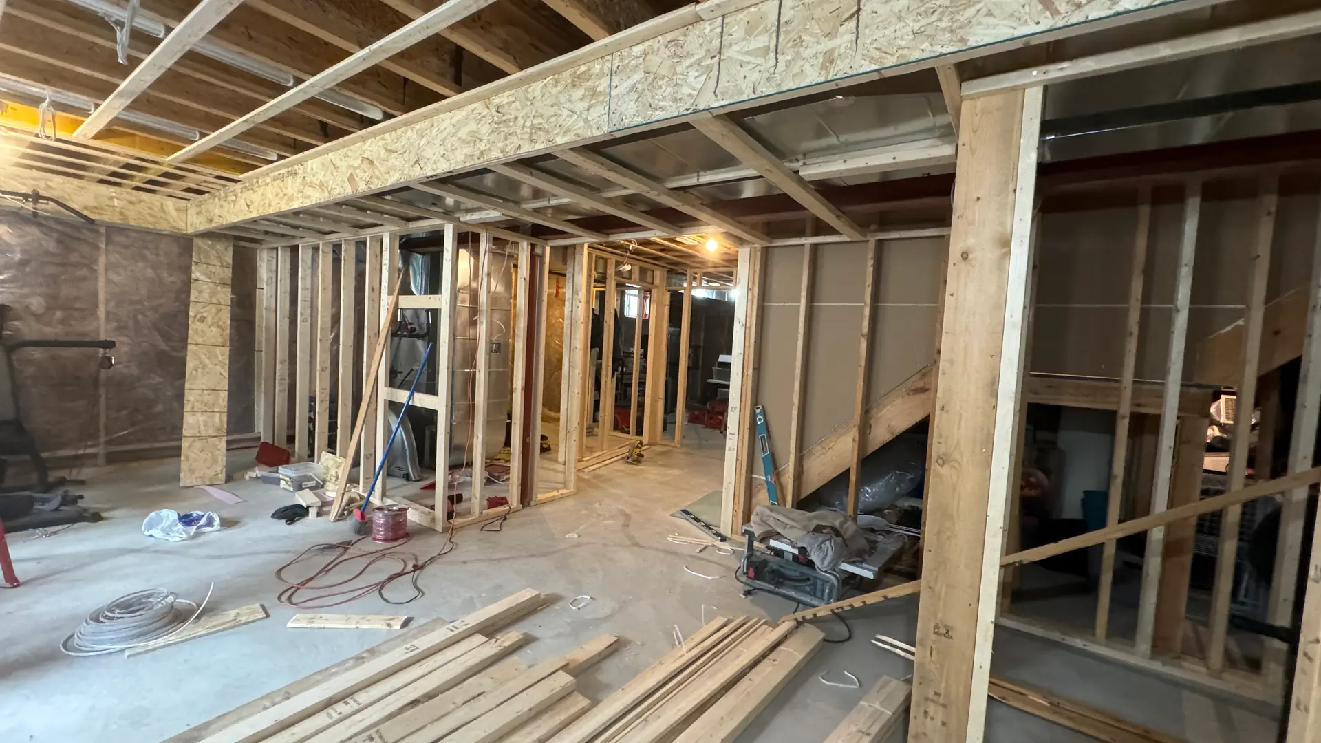 Sous-sol en rénovation avec ossature en bois, câblage électrique, et travaux de finition en cours.