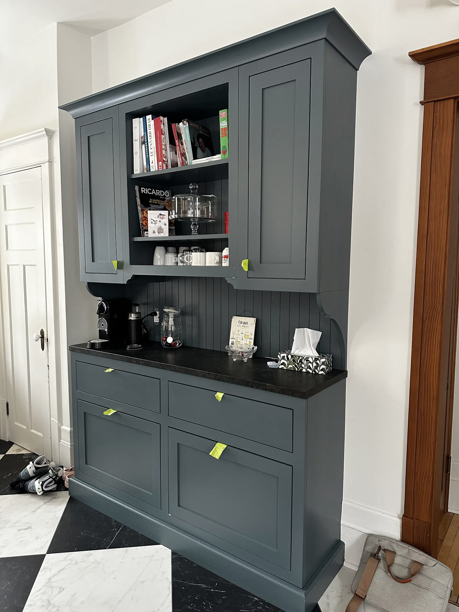 Dark grey built-in cabinet with a black countertop, open shelving, coffee maker, and dishes.