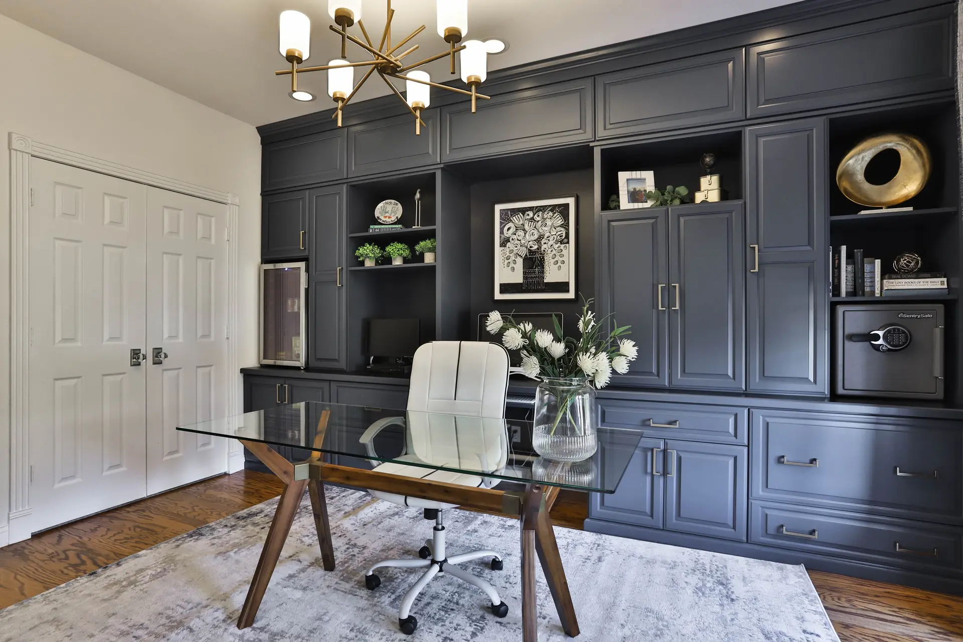 Modern home office with dark blue built-in cabinetry, custom bookshelf, glass desk and contemporary lighting
