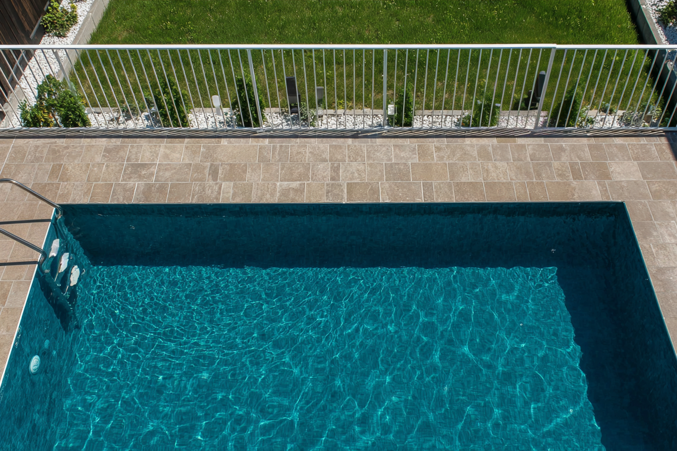 Inground pool with stone coping and white aluminum safety fence in a landscaped residential yard