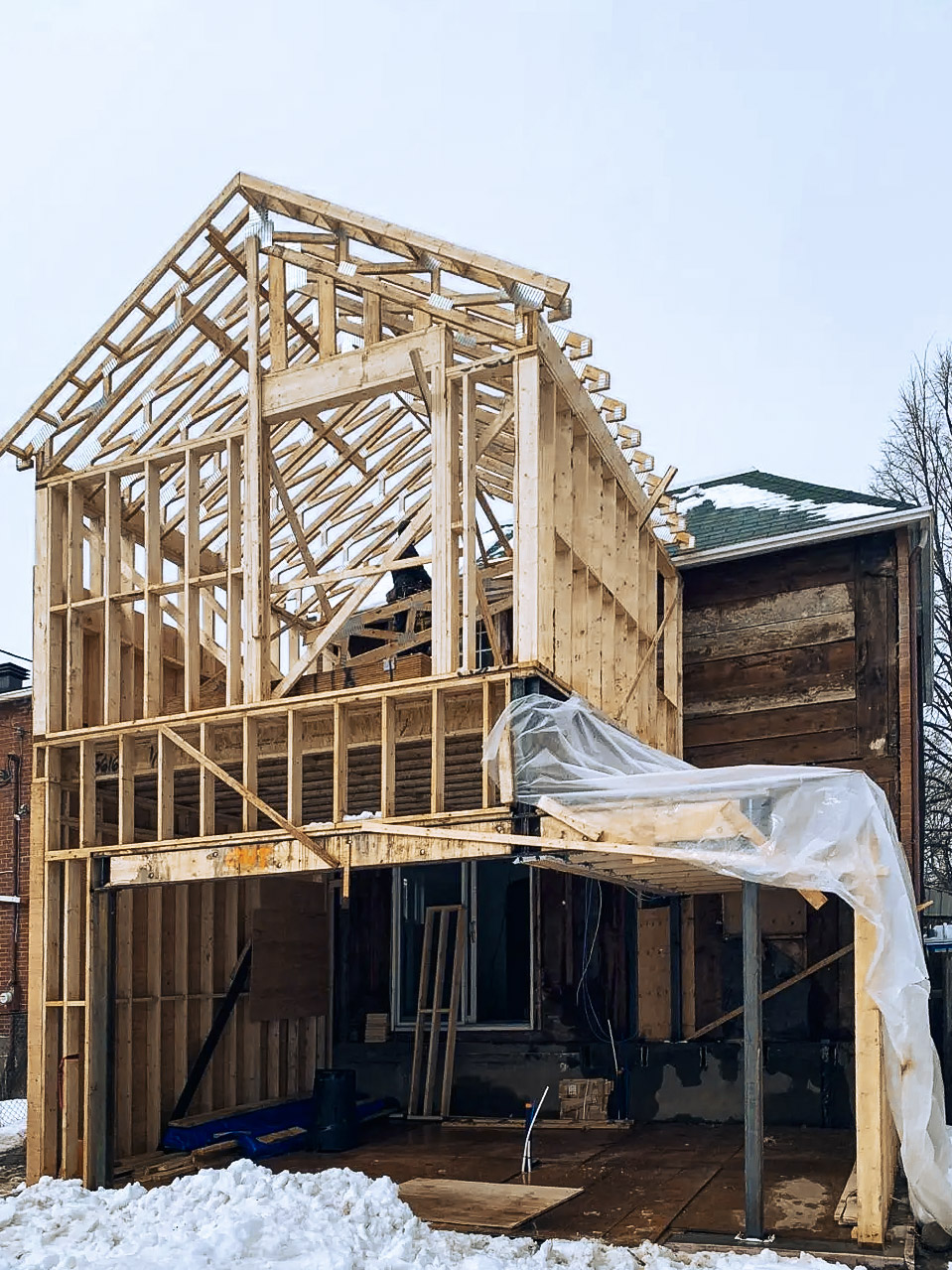 Structure en bois d’une maison en rénovation avec charpente de toit apparente, murs ouverts et agrandissement en construction pendant l’hiver.