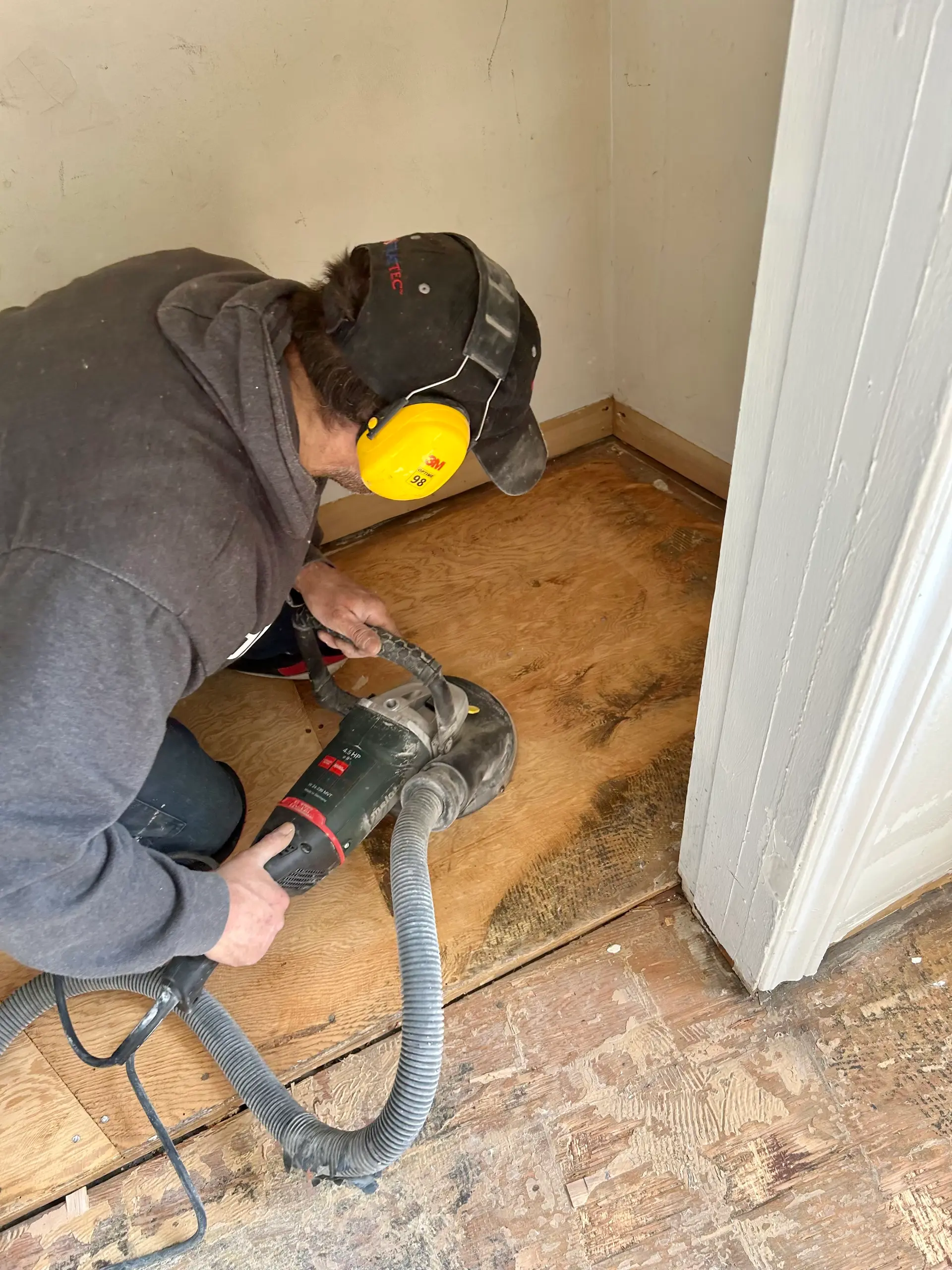 Travailleur sablant un plancher de bois avec une ponceuse munie d’un tuyau d’aspiration pour réduire la poussière.
