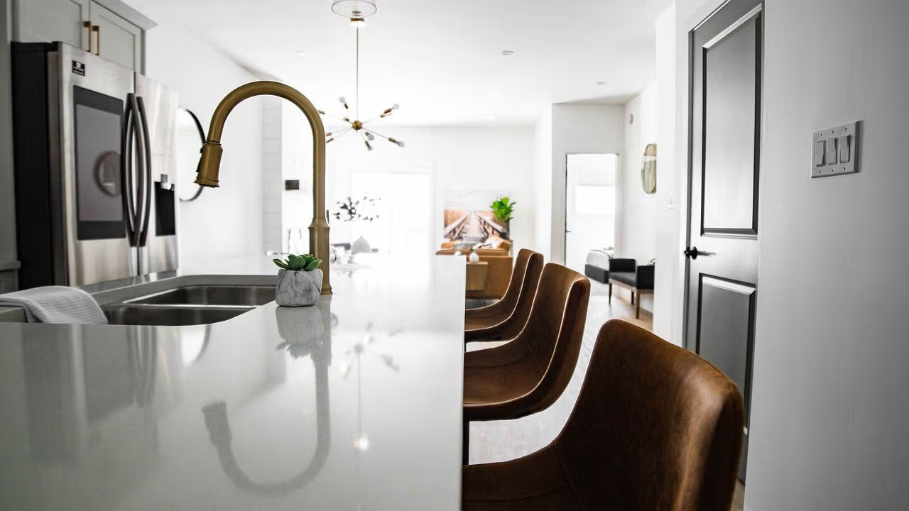 Bright modern kitchen with white island, gold faucet, brown leather chairs and contemporary open-concept layout