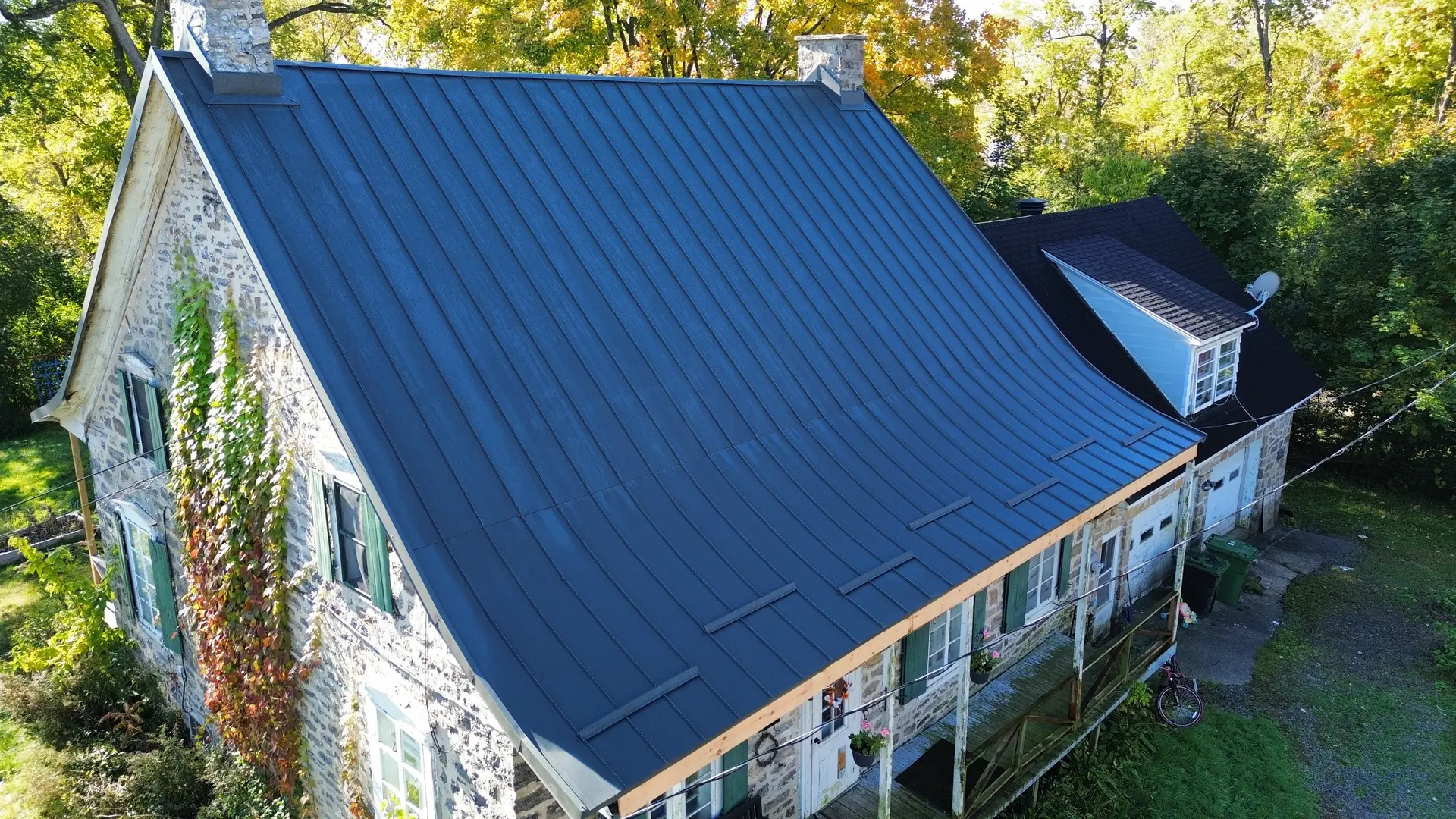 Blue metal roof on a historic stone house with climbing ivy, surrounded by autumn trees.
