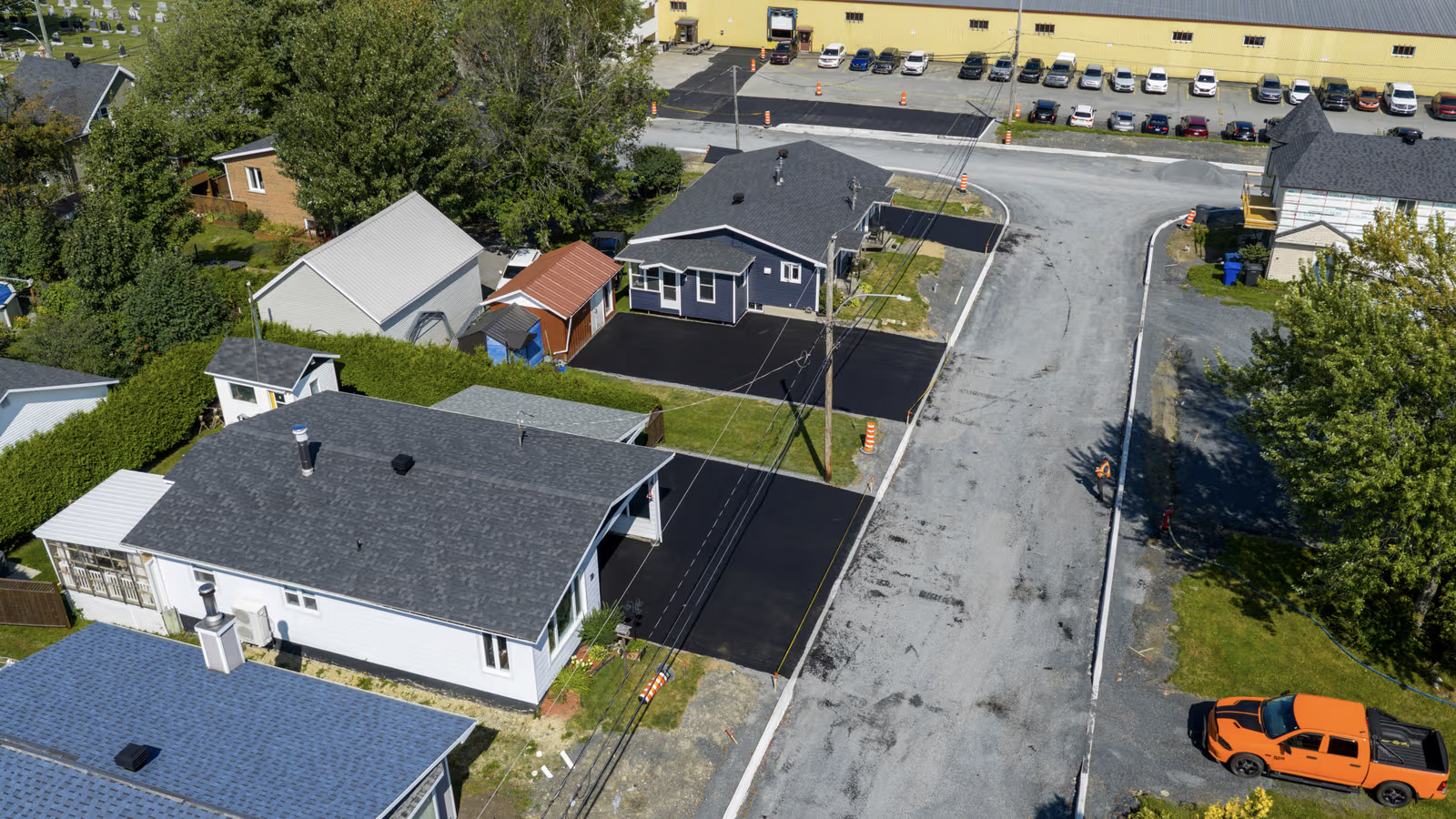 Vue aérienne d’un quartier résidentiel montrant des entrées fraîchement asphaltées, une rue en réfection et des cônes de chantier.