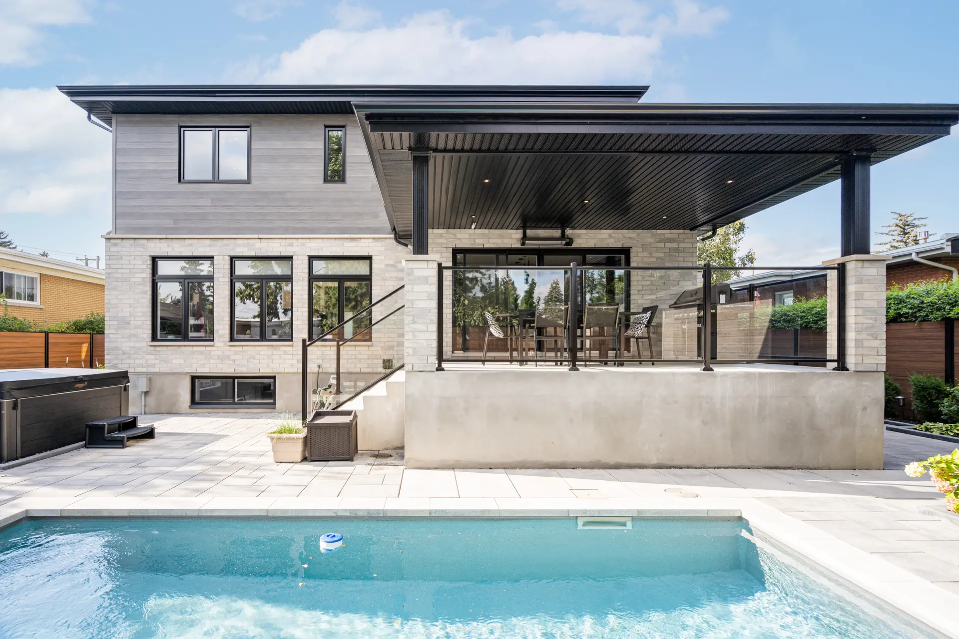 Modern house with covered terrace, glass railing, inground pool and landscaped backyard