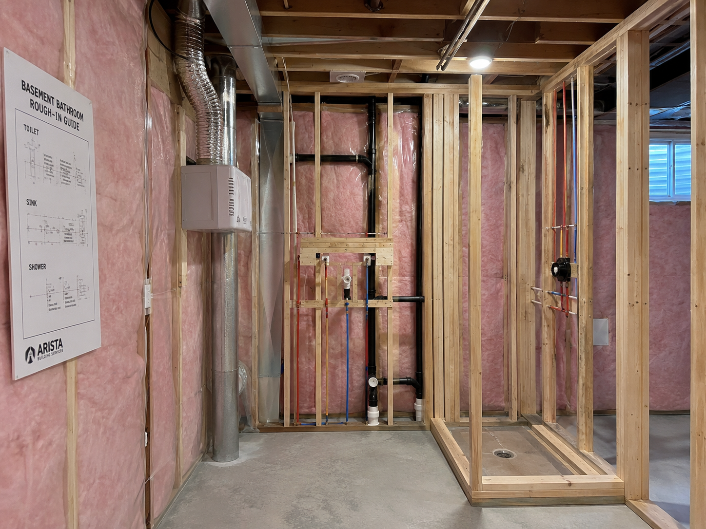 Salle de bain de sous-sol en construction avec ossature en bois, isolation en fibre de verre, plomberie apparente, conduits de ventilation et plan de raccordement affiché