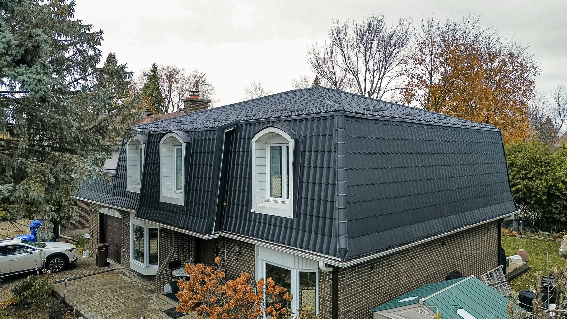 Maison en briques avec toiture en tôle noire style tuiles, lucarnes blanches.