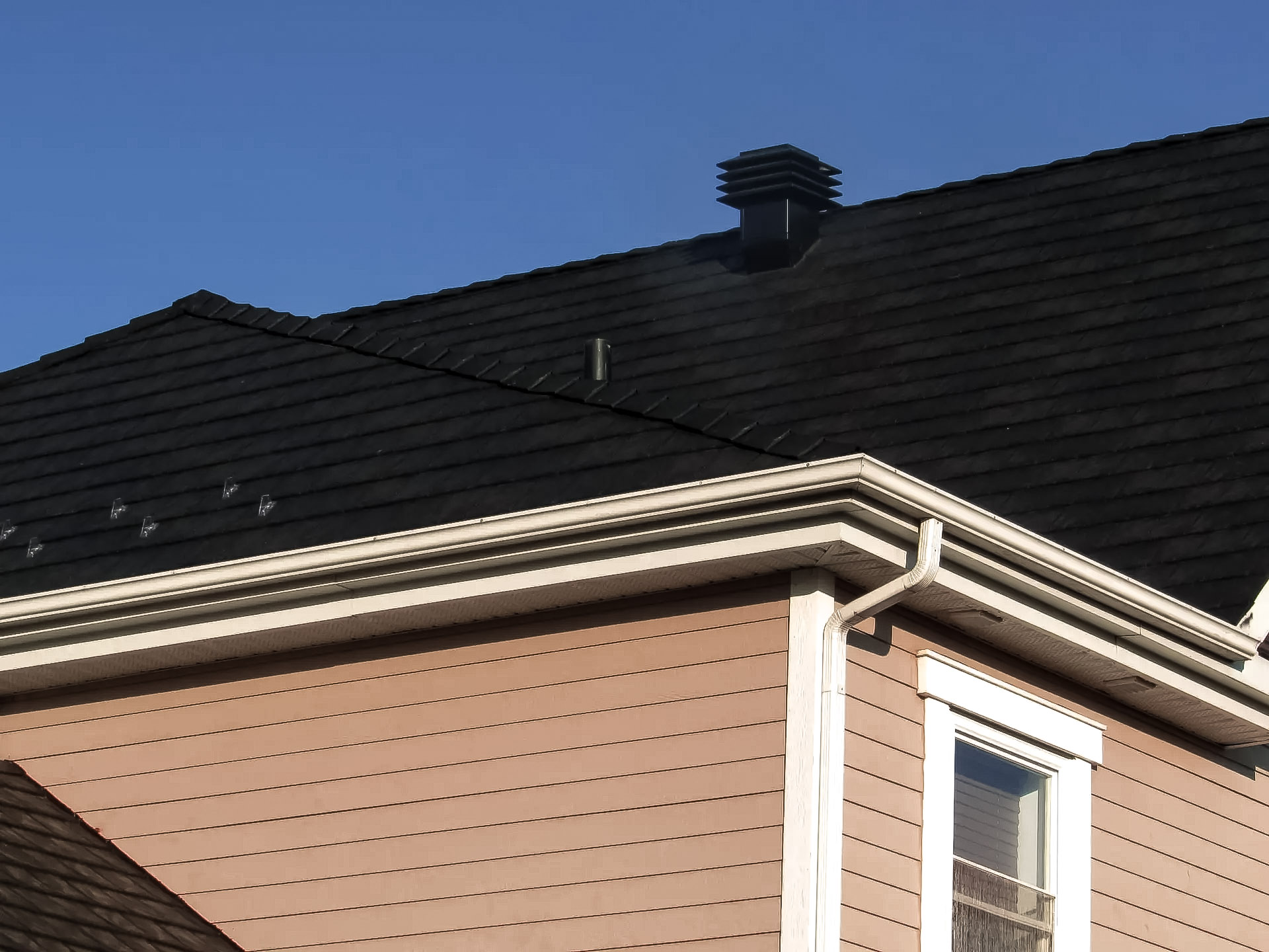 &nbsp;Toiture en bardeaux noirs avec ventilation et gouttières blanches sur une maison en revêtement jaune.