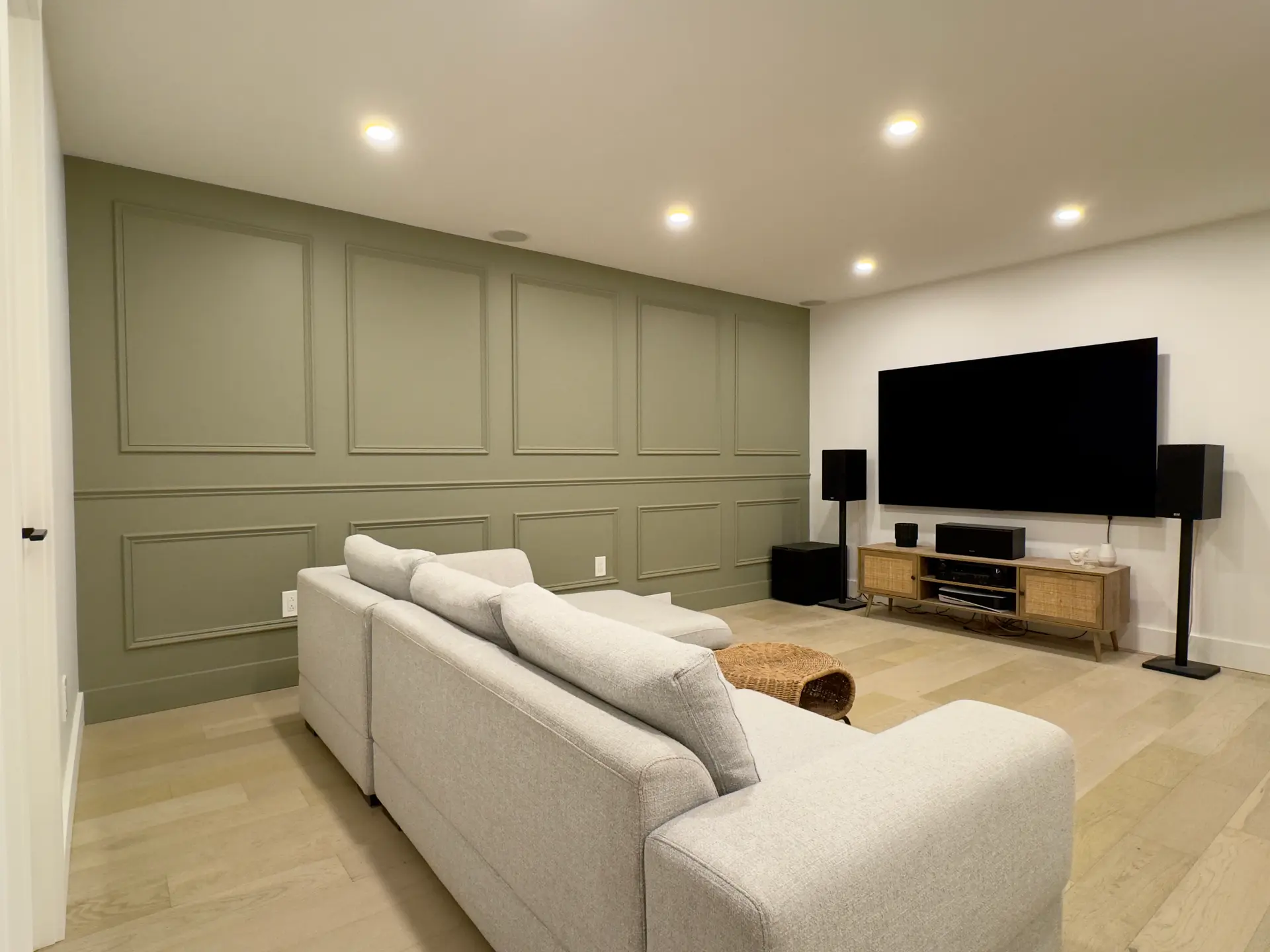Modern living room with a green accent wall, a large gray sofa, a flat-screen TV, and an audio system.