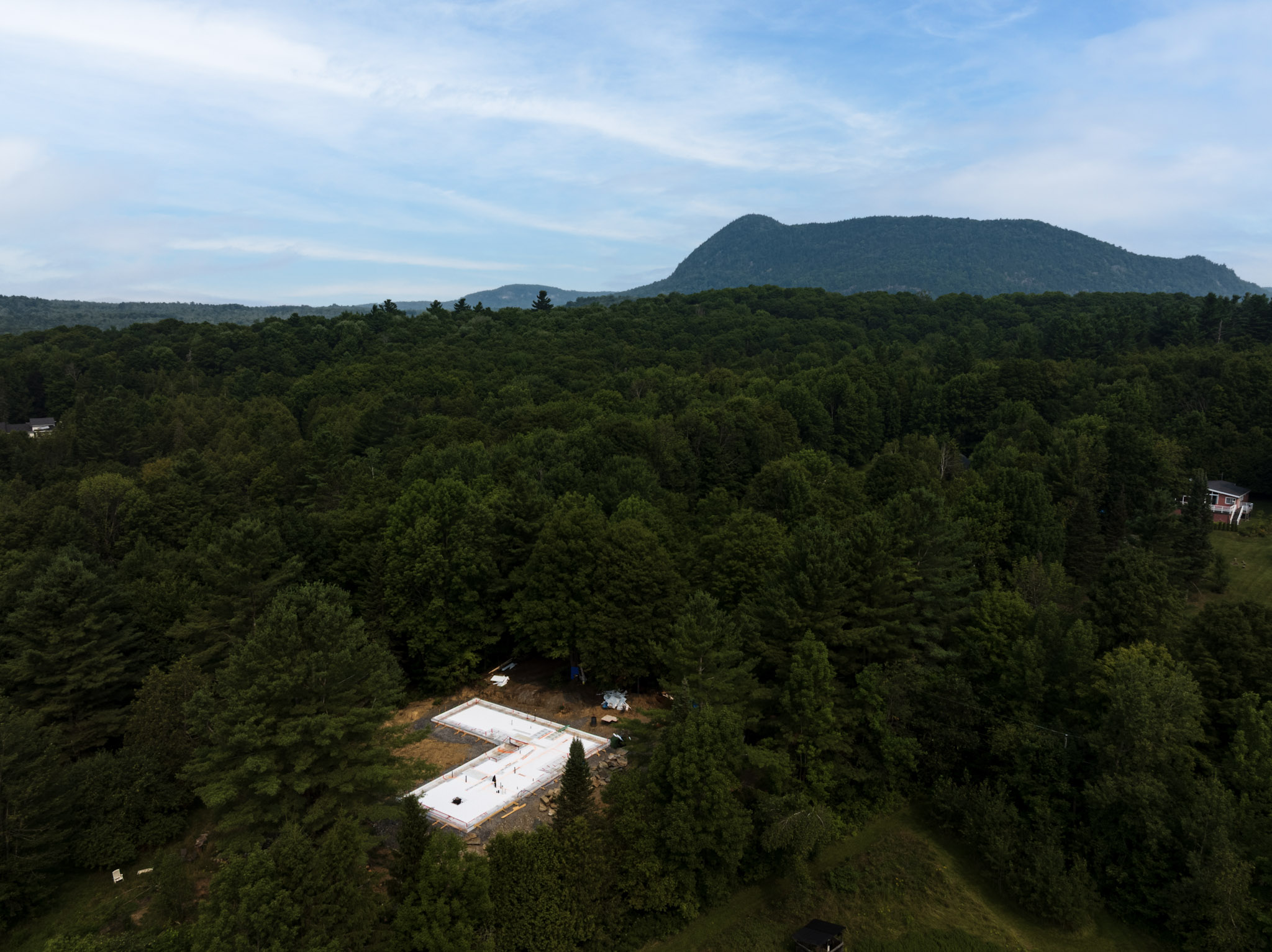 Aerial view of a house foundation under construction in the heart of a forest with mountains in the background